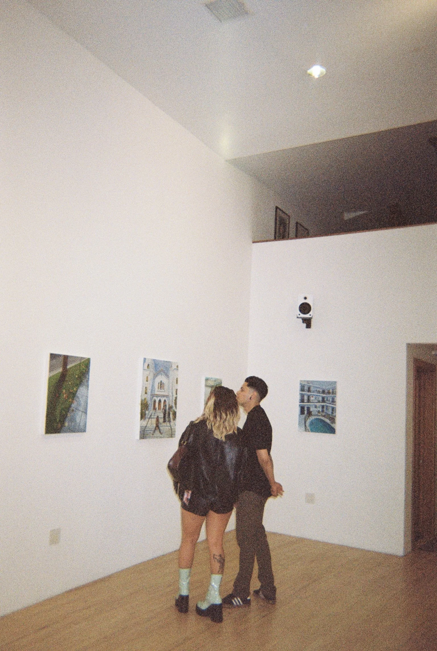 Two people standing close together in an art gallery with framed pictures on white walls.