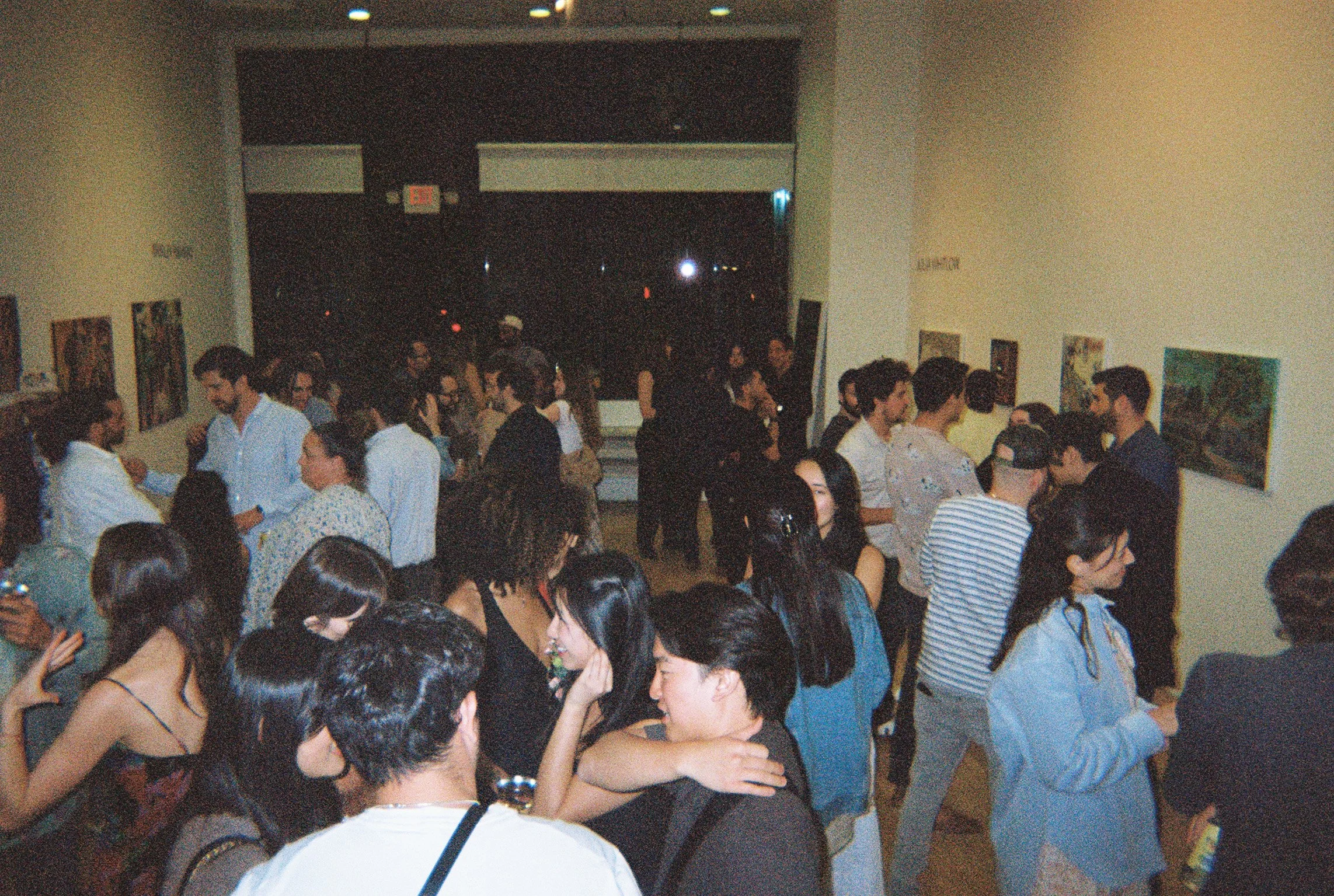 Crowd of people socializing at an art gallery during an evening event.