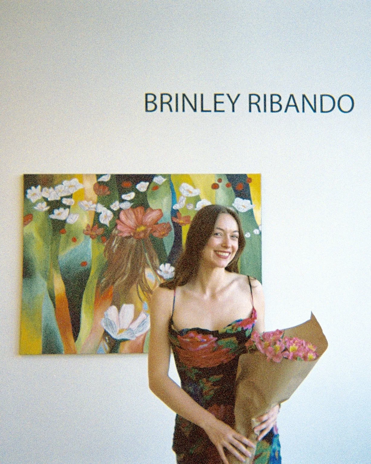An art gallery with a woman holding a bouquet of pink flowers in front of a colorful painting. The gallery has the name 'Brinley Ribando' displayed on the wall.