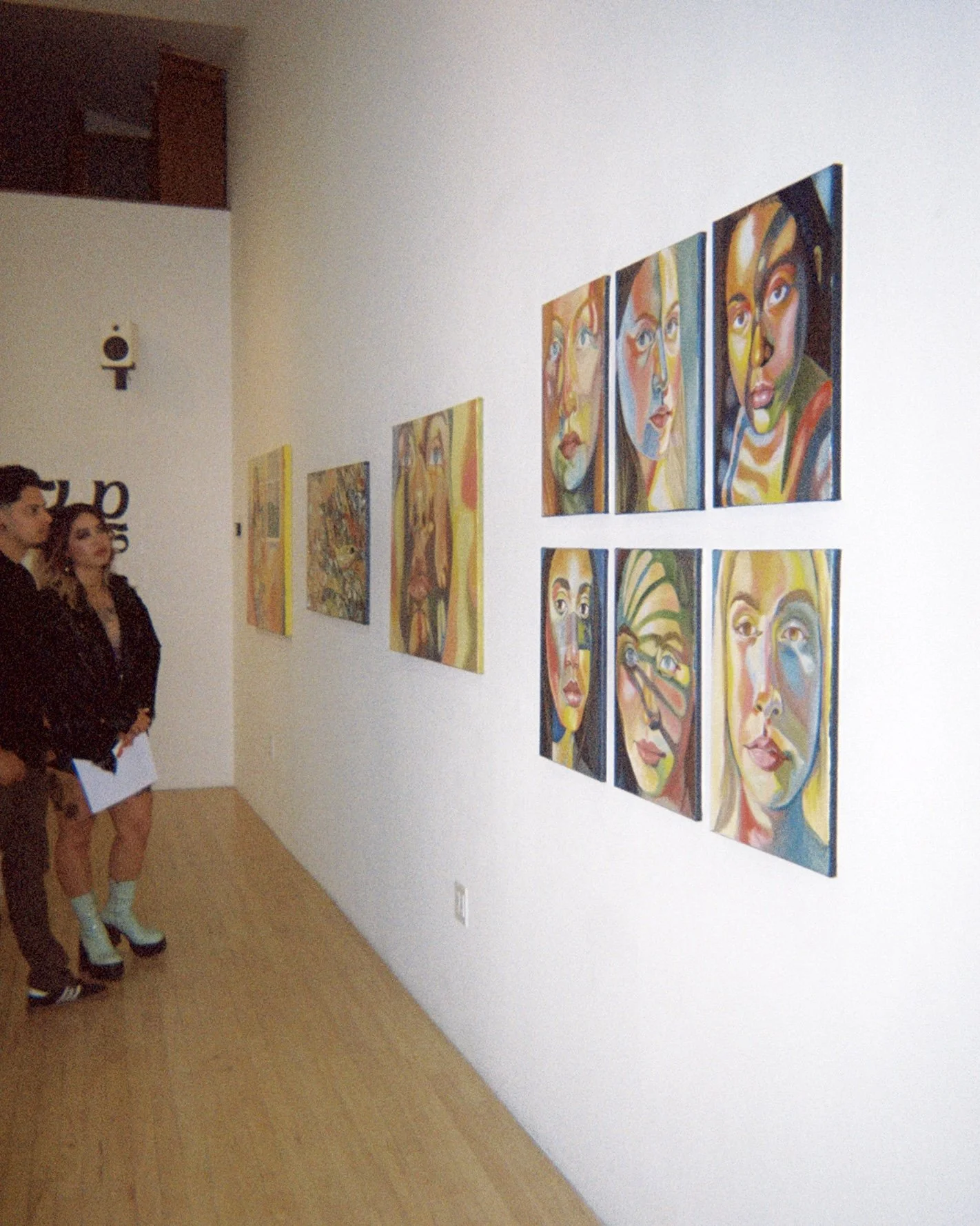 Two people observing colorful paintings in an art gallery.