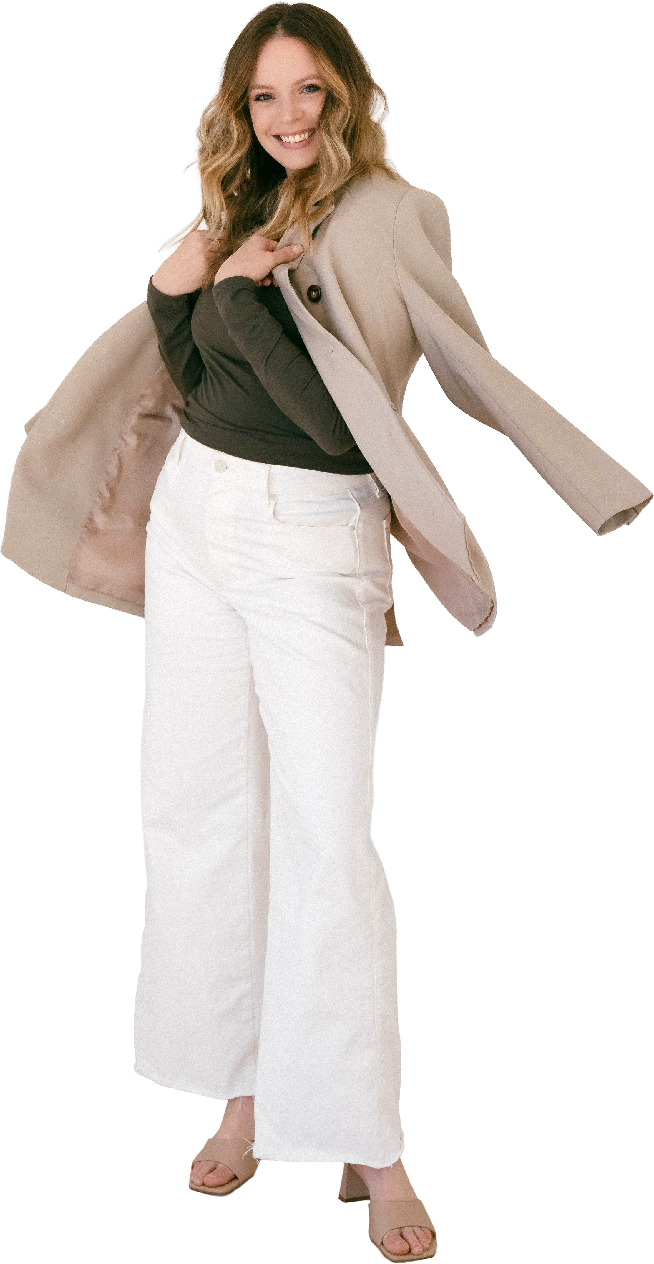 Courtney Slate, a woman with long wavy hair smiling, wearing a beige coat draped over her shoulders, a dark green top, white high-waisted wide-leg jeans, and beige sandals.