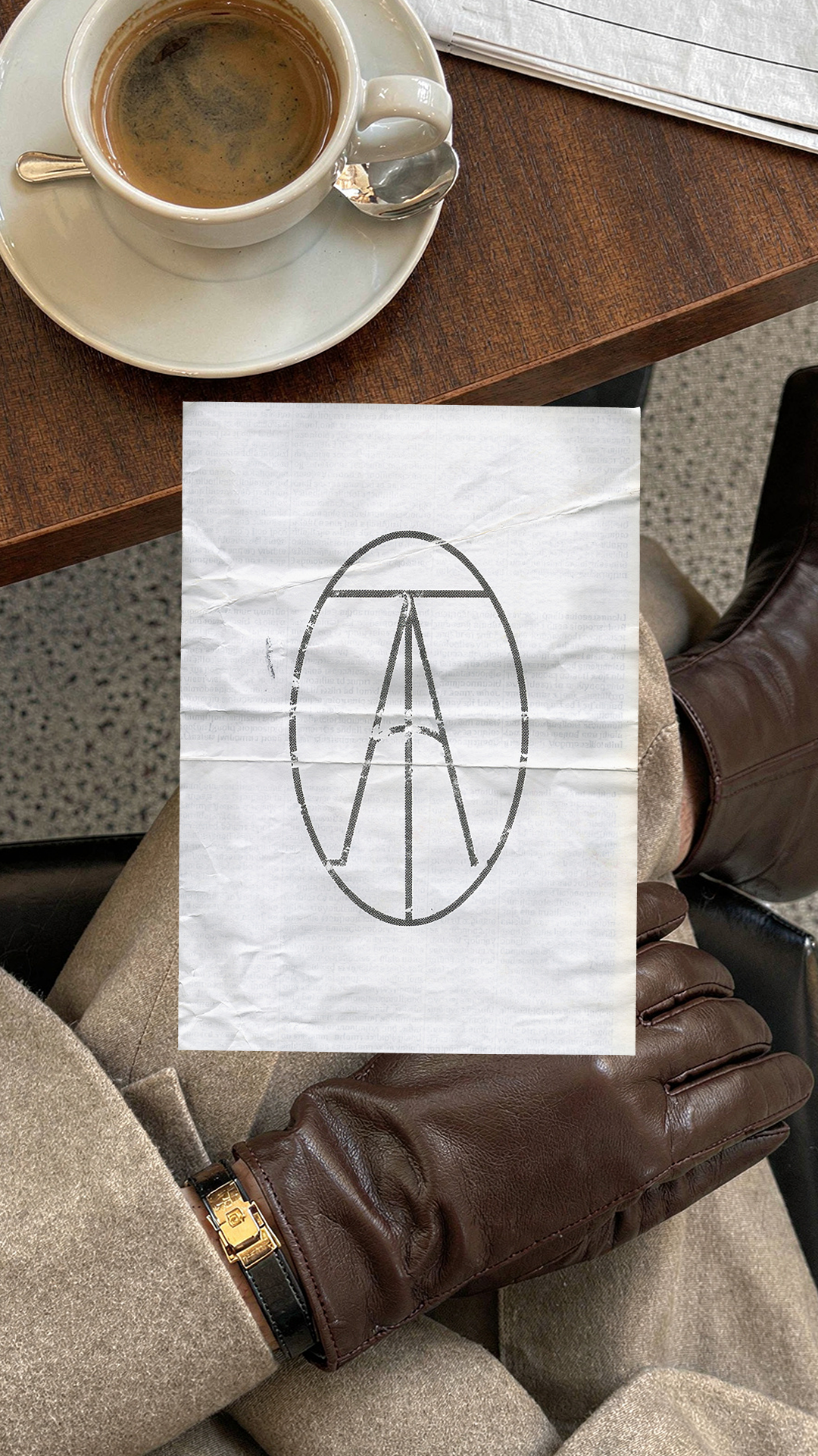 The Archive Creative Agency oval monogram printed on crinkled paper, held over coffee and leather gloves