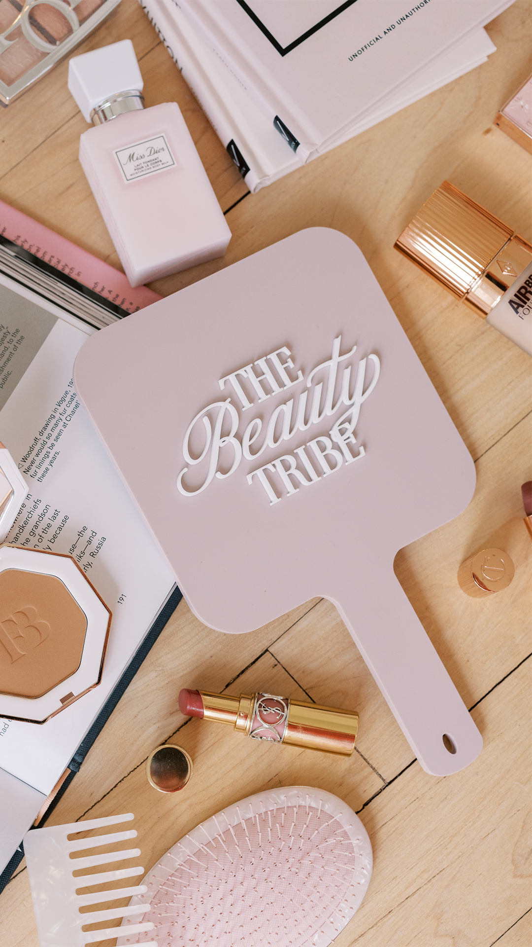 Blush hand mirror with The Beauty Tribe logo styled with luxury makeup and hair brushes, bridal beauty brand flat lay