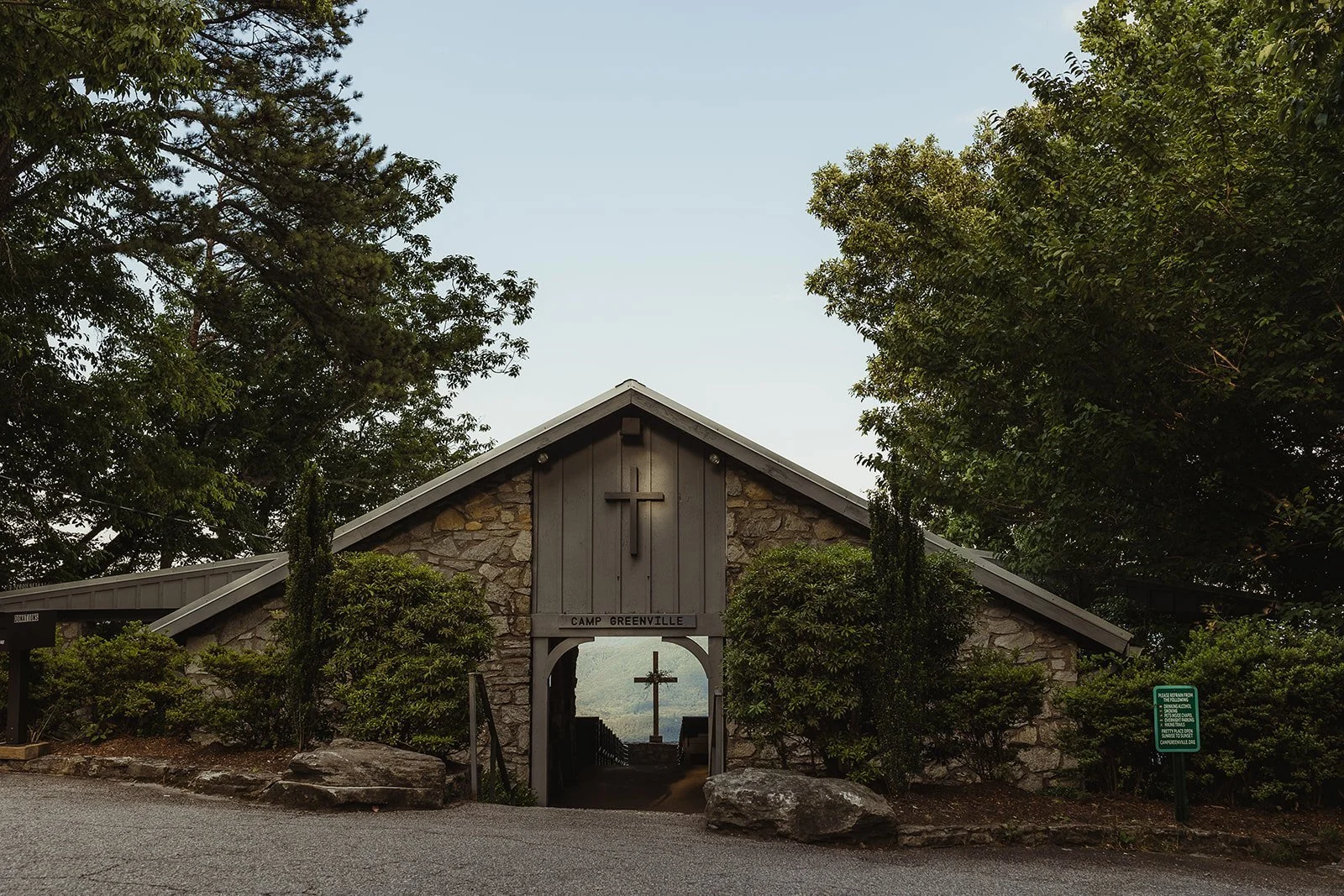 Outdoor chapel with wooden cross, benches, and a view of misty mountains at sunrise. The phrase 'I will lift up mine eyes unto the hills' is displayed above.