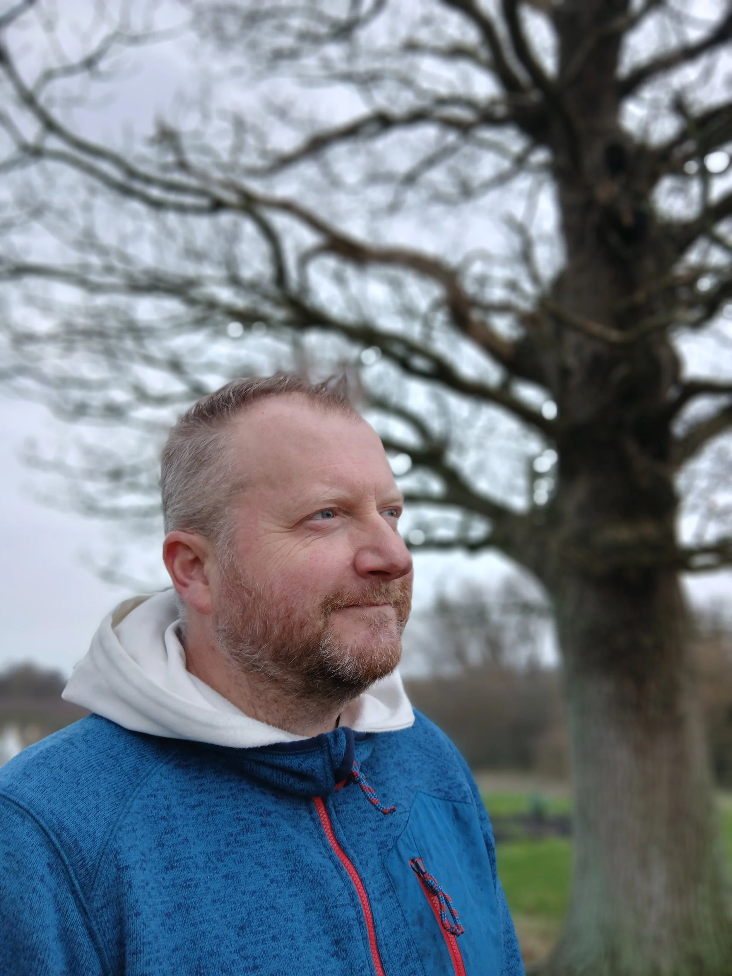 Alex Vrettos, Therapeutic Hypnotist, looking thoughtfully off to camera right with a tree in the background