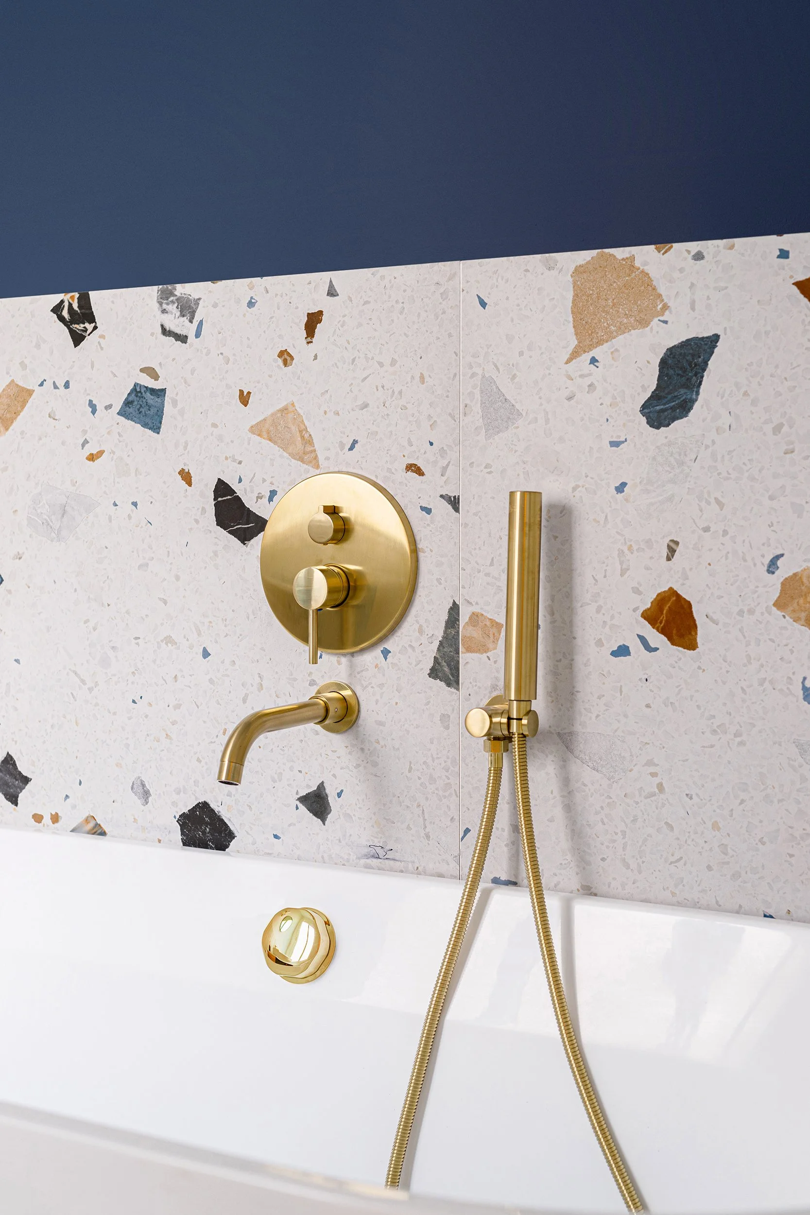 Bathroom with terrazzo tiles, brass fixtures, and bathtub faucet.