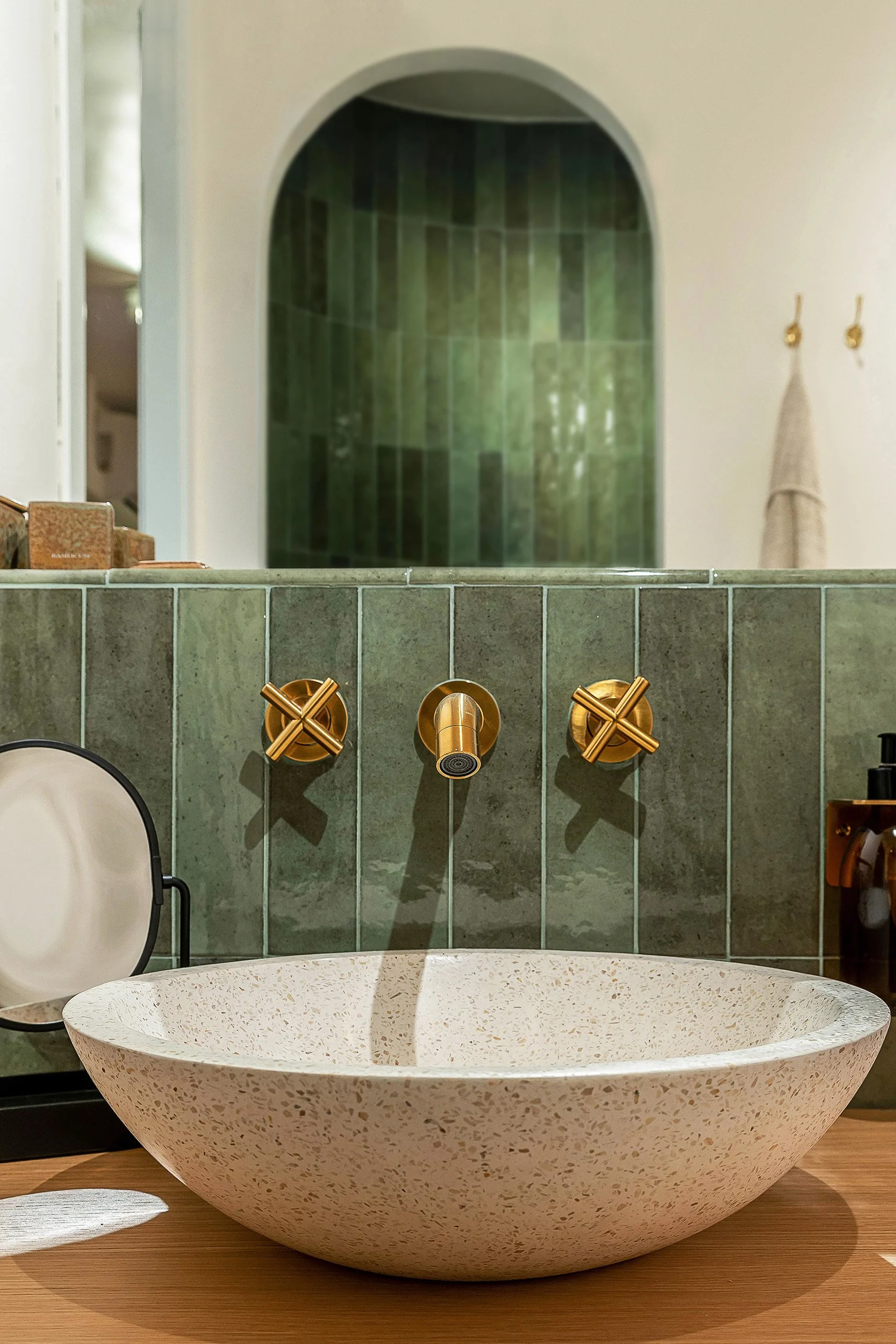 Modern bathroom with green tile backsplash, gold faucet and handles, and a round speckled stone sink.