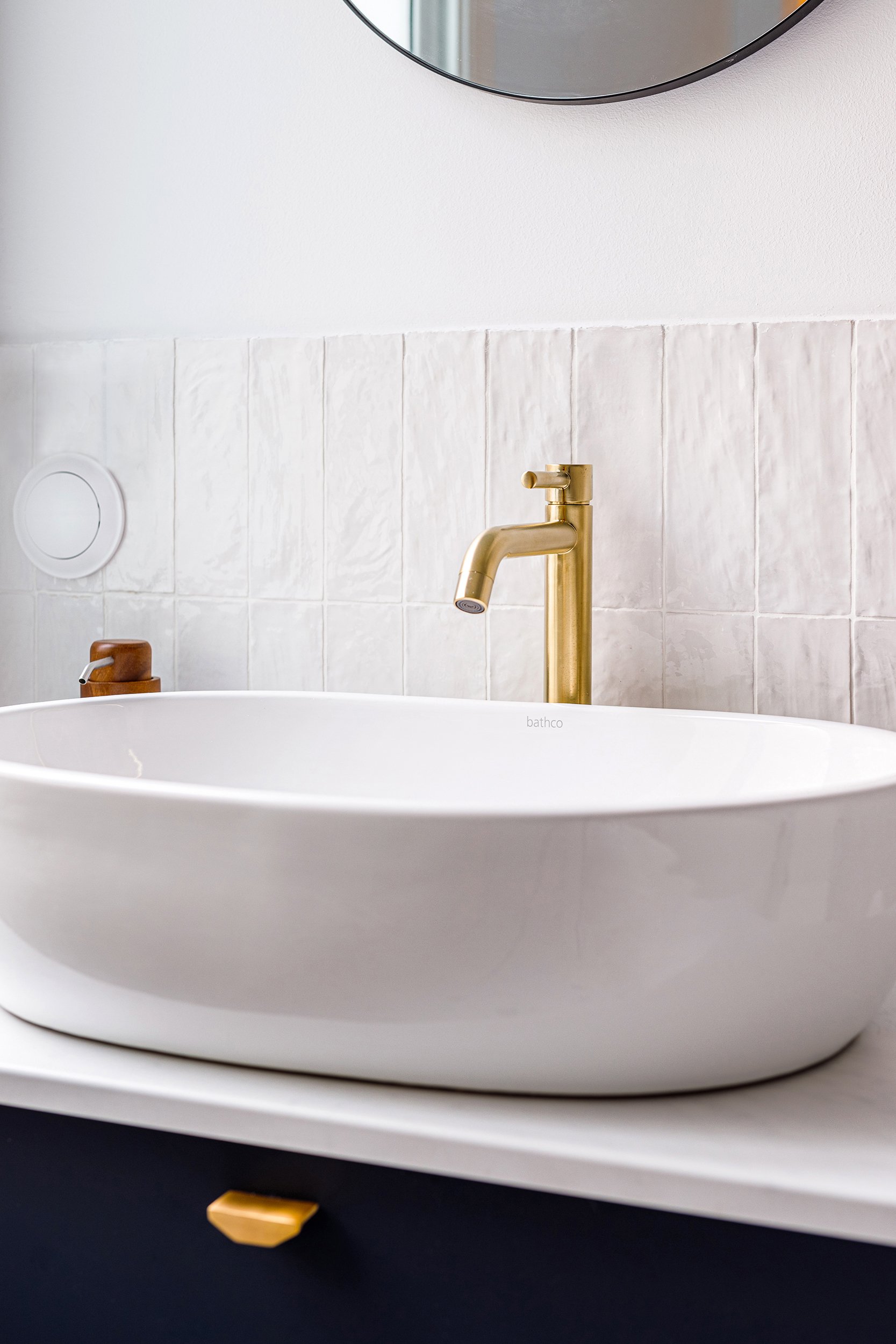 Modern bathroom sink with a gold faucet and white tile backsplash.