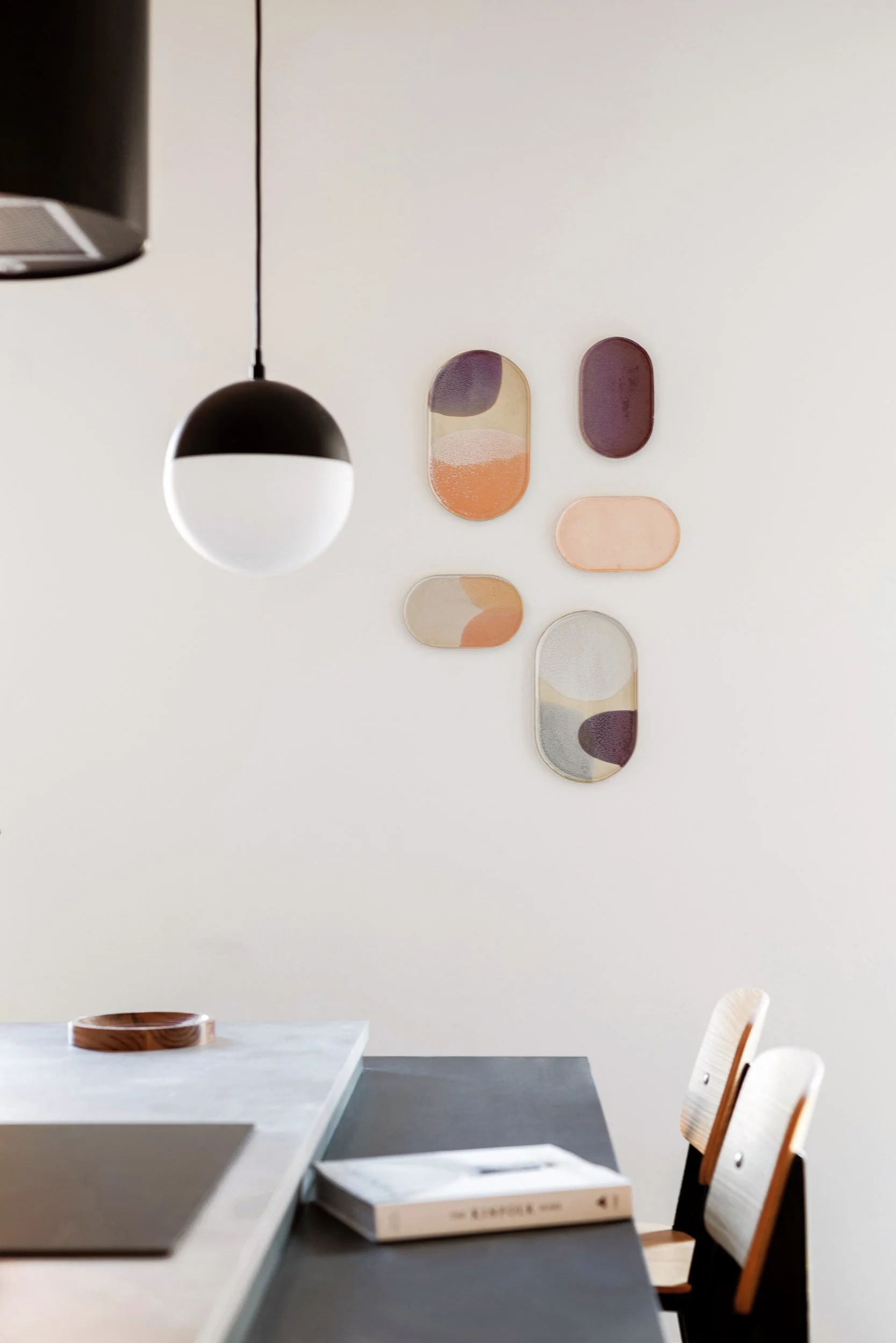 Modern dining area with a black and white pendant light, abstract wall art, wooden chairs, and a book on the table.