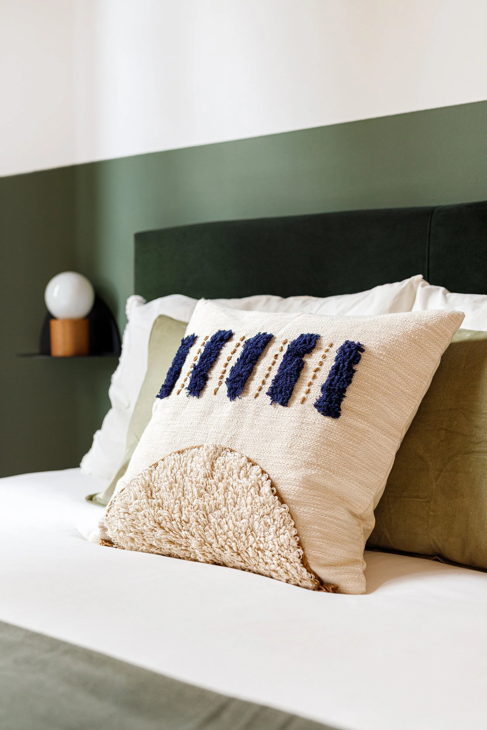 Decorative pillows on a bed with a modern lamp on a shelf in the background.