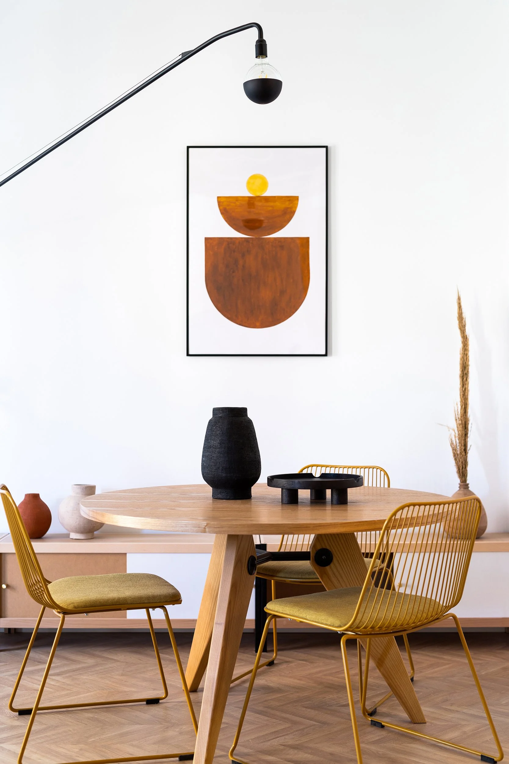 Minimalist dining room with wooden table, yellow wire chairs, abstract wall art, and modern floor lamp.