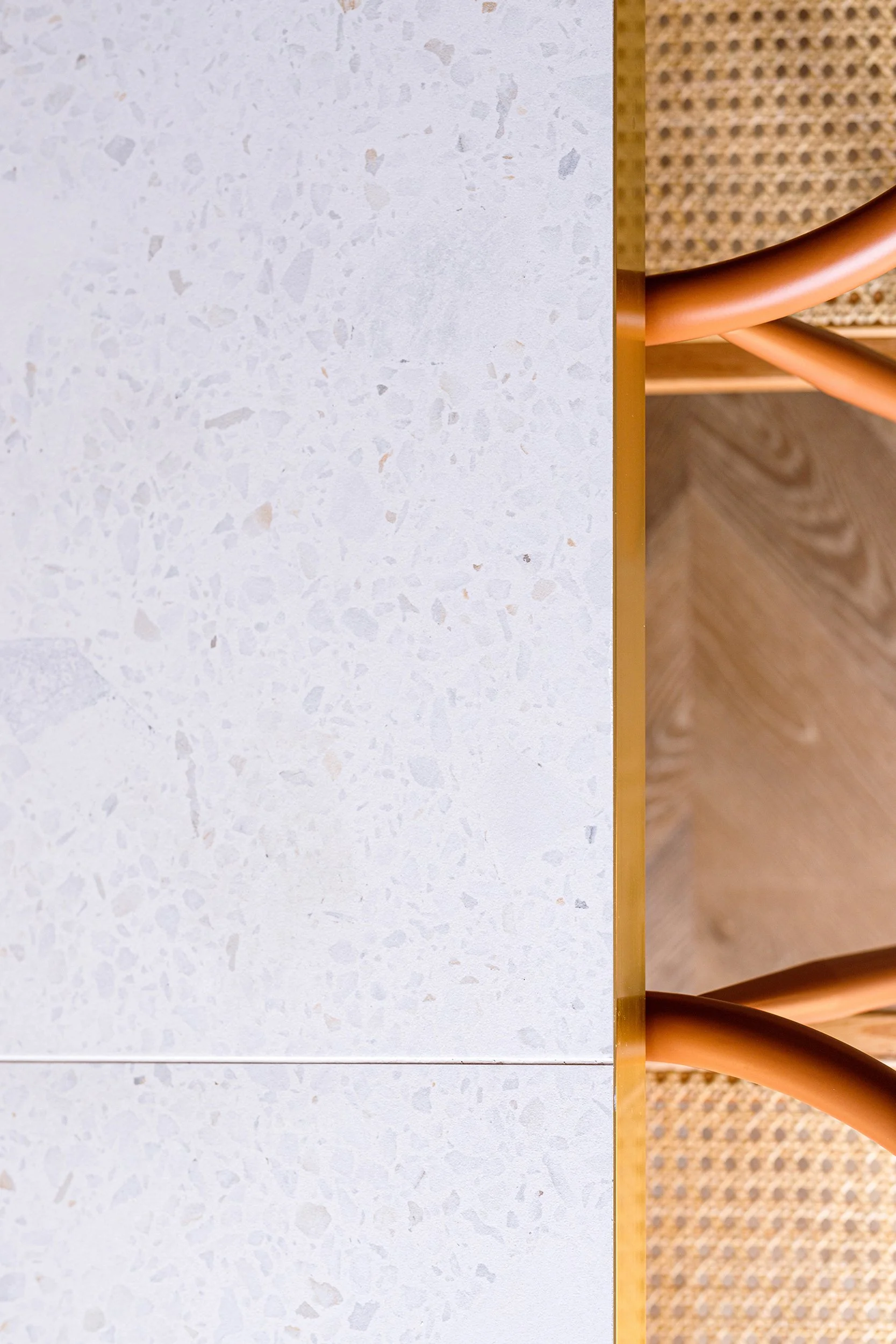 Overhead view of a terrazzo table next to a woven cane chair with wooden frame.