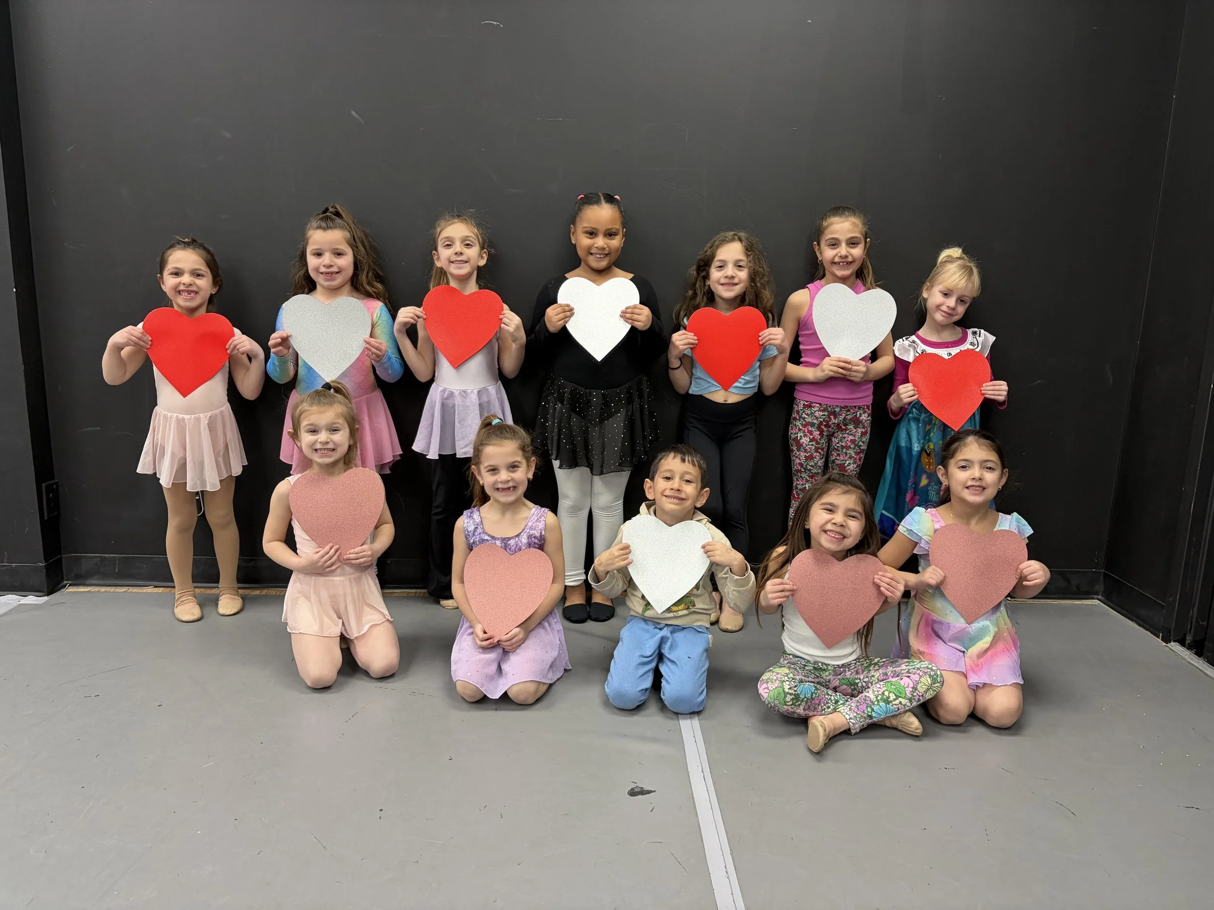 DXNY Dance older students and young dancers sitting together on the studio floor making.Valentine's Day heart crafts