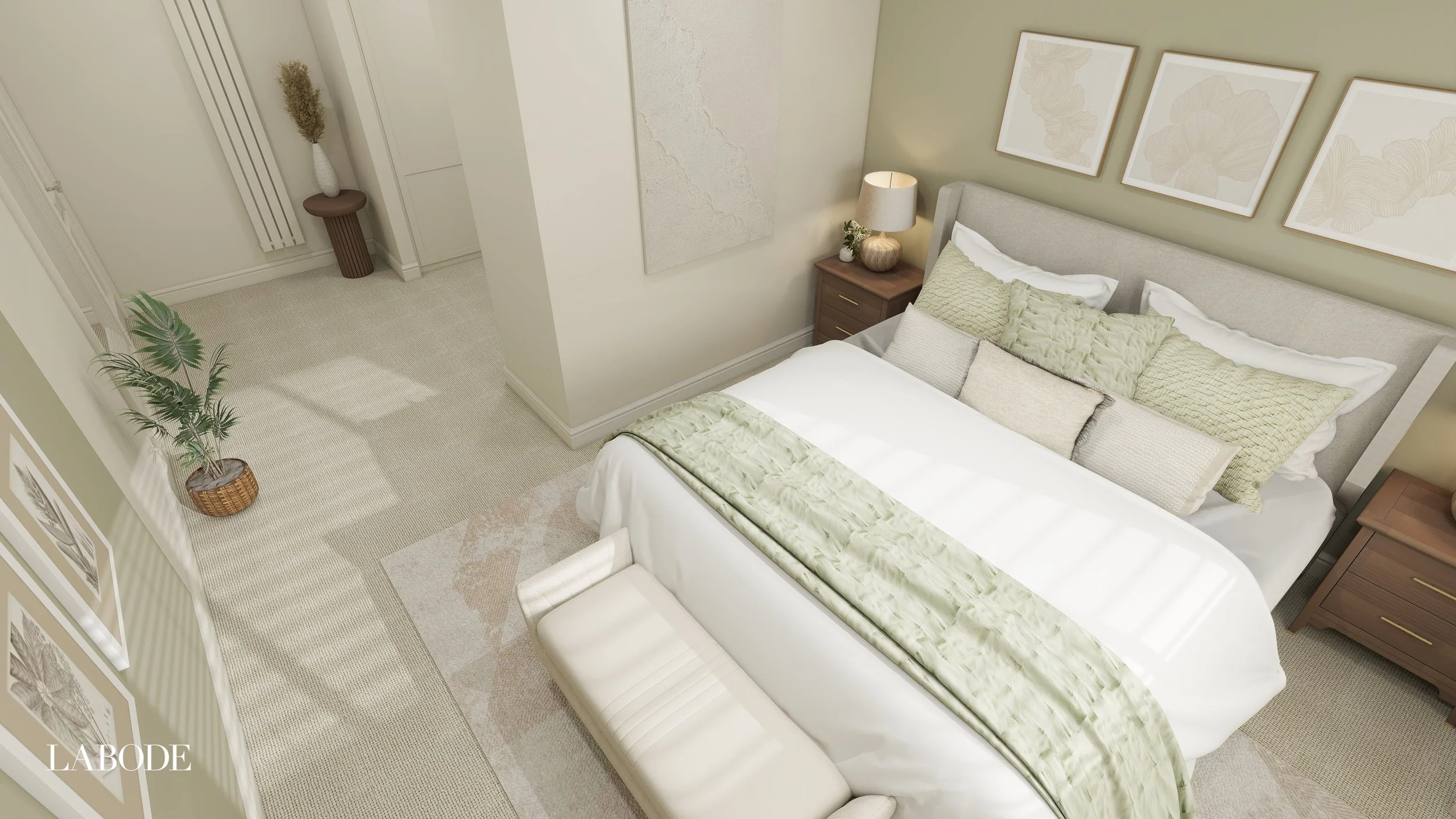 A neatly made bed with light green and beige pillows, a beige headboard, and a matching green bed runner in a cozy bedroom. Beside the bed is a wooden nightstand with a lamp and a small plant. The wall above the bed has three framed botanical prints. There is a large potted plant on the floor near the corner, and a tall vase with dried flowers on a small round table in the corner of the room. The room has light-colored walls and carpeted flooring.
