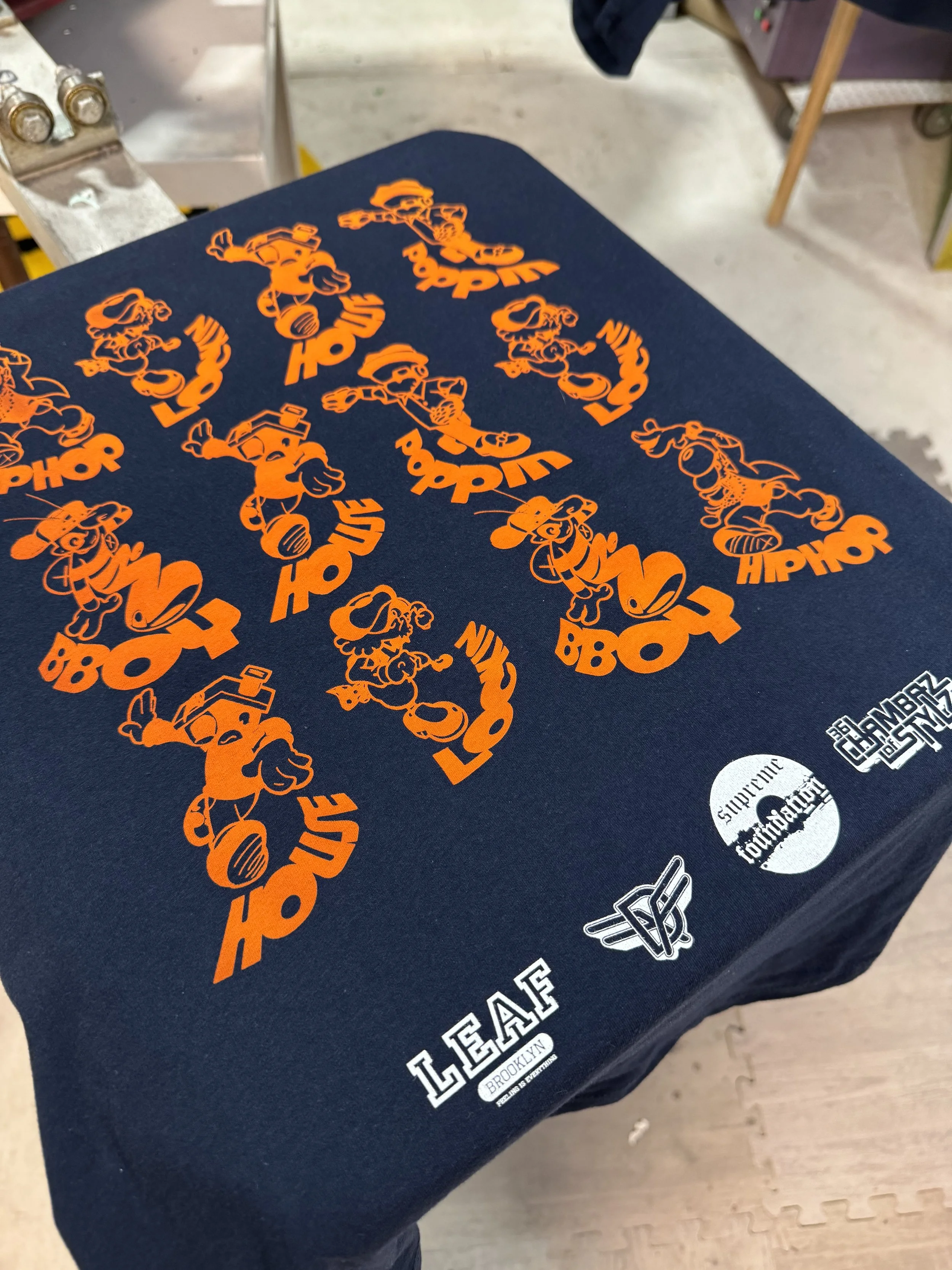 A dark blue tablecloth with orange stickers of cartoon characters and text, including 'LEAF' and 'BROOKLYN'.