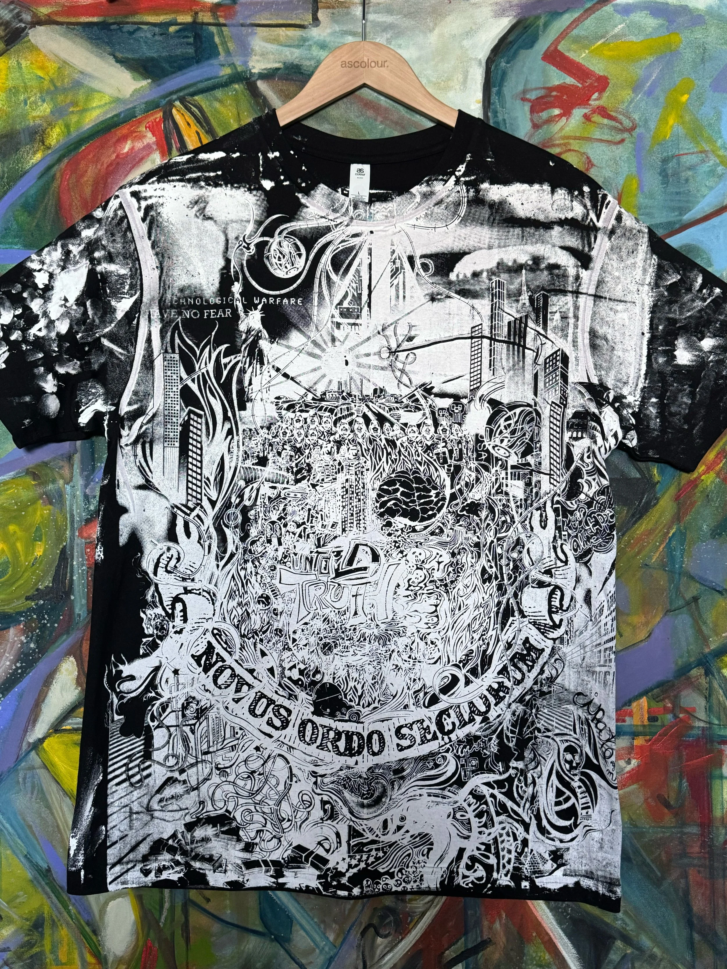 Black and white graphic t-shirt with intricate urban, sci-fi, and abstract designs, hanging on a wooden hanger against a colorful, graffiti-style painted background.