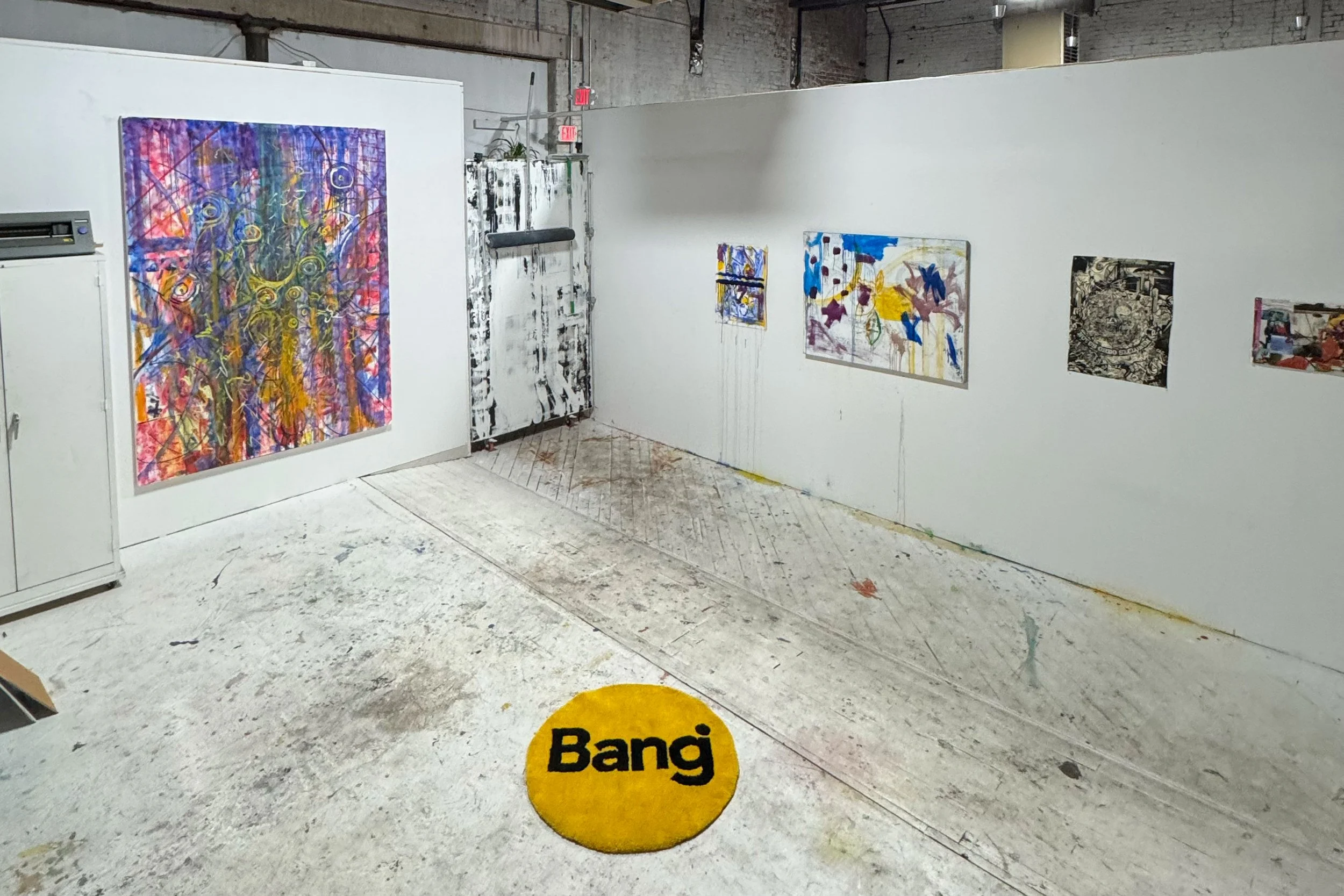 An art gallery with abstract paintings on white walls. The floor is painted concrete with a yellow round sign that says 'Bang'.