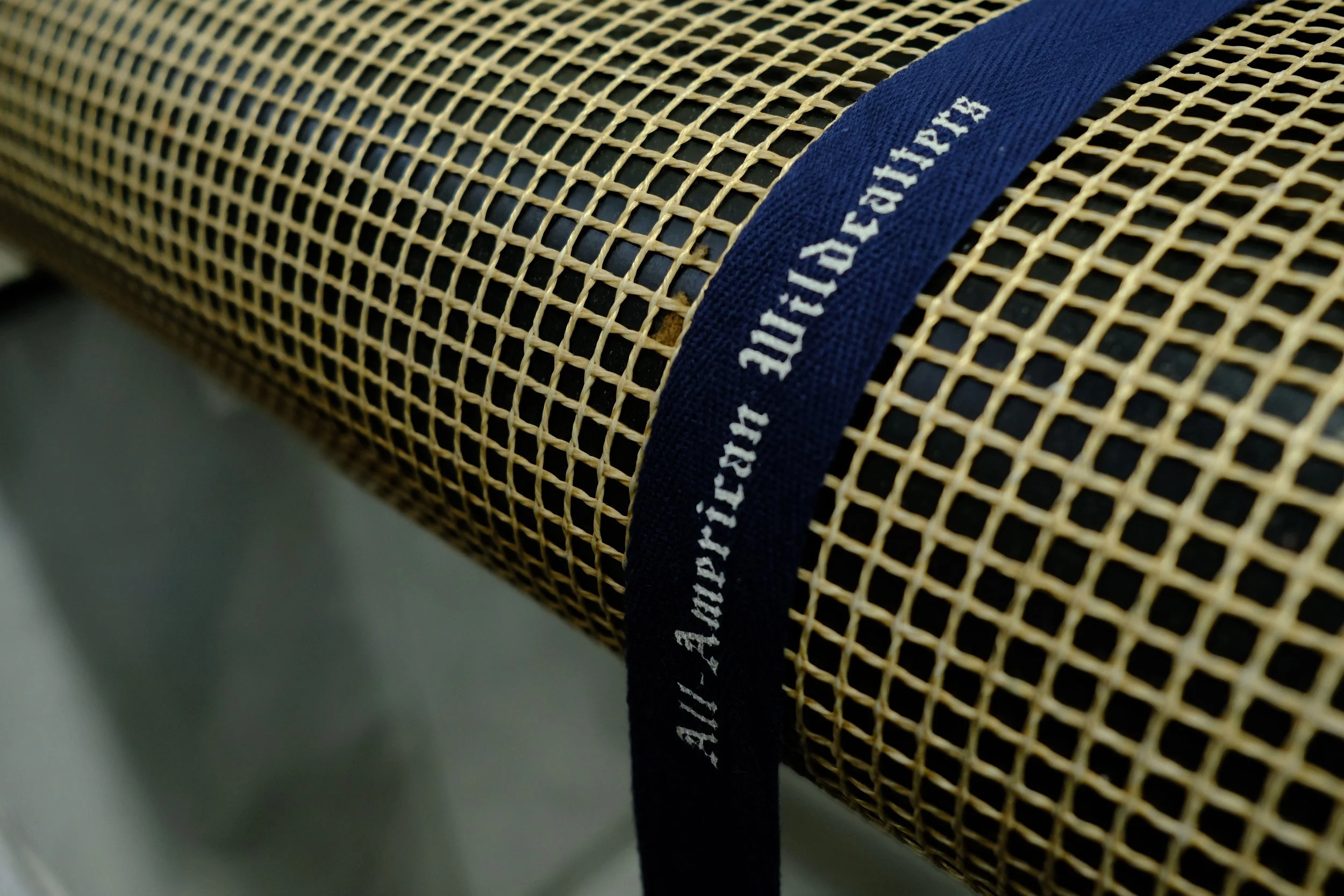Close-up of a yellow perforated metal surface with a blue fabric strap across it. The strap has white text, but only part of it is visible.