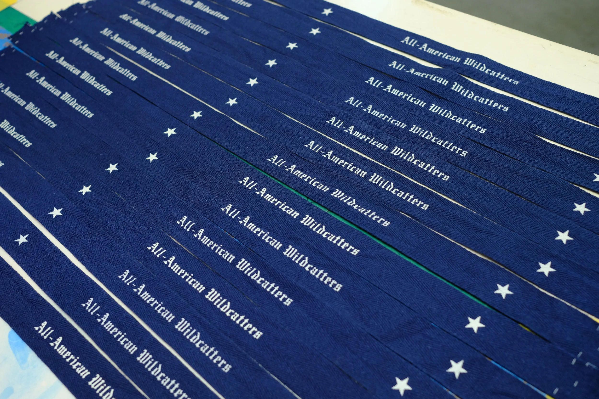Stacked dark blue fabric strips with white stars and the text 'All-American Wildcatters' printed on each strip.