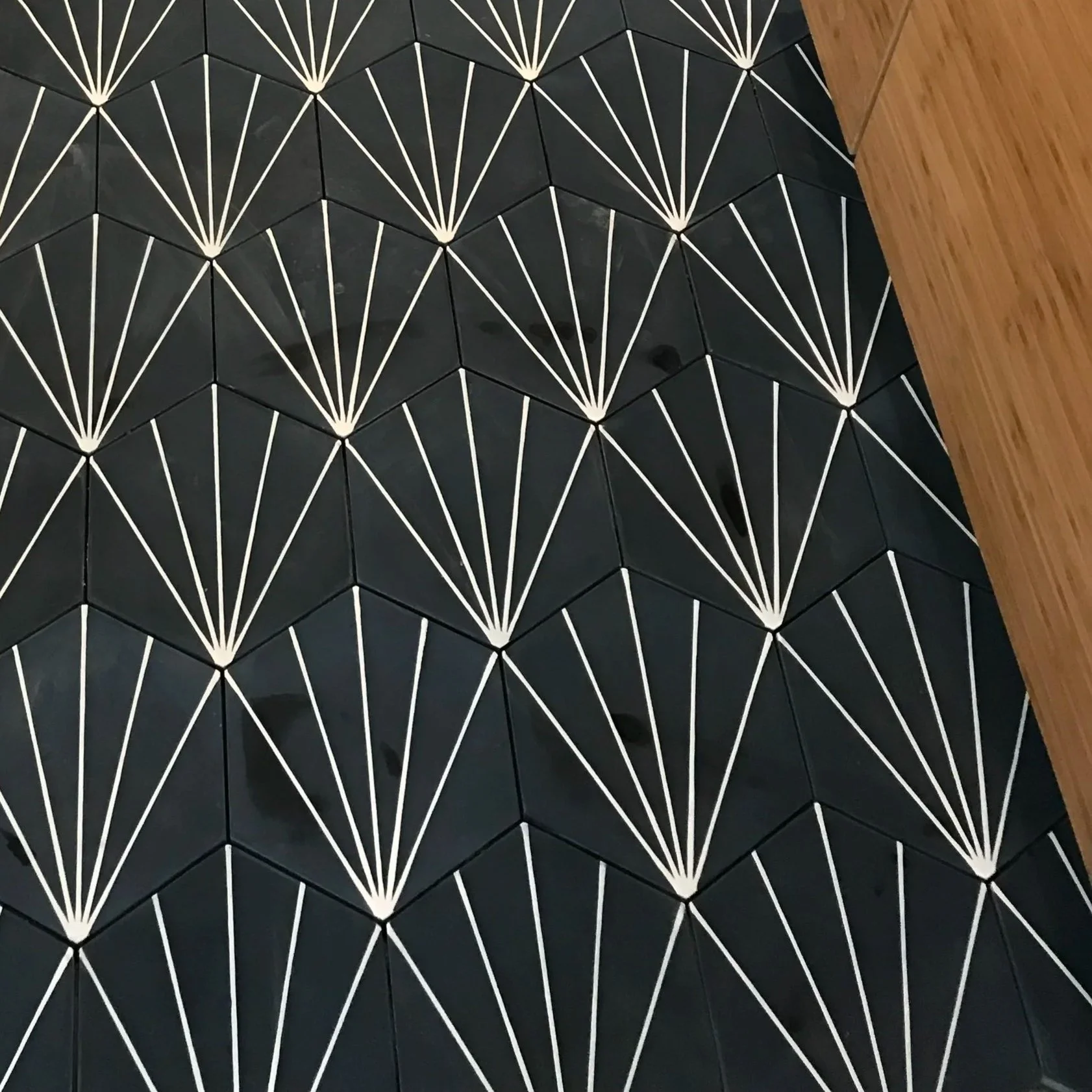 Close-up of a black geometric wall with white lines forming a repeating fan-shaped pattern, next to a wooden surface.