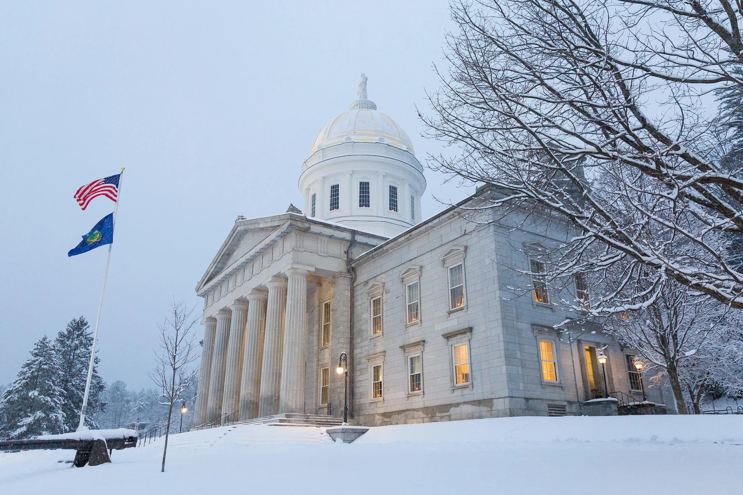 Vermont State House in winter with US and state flag.