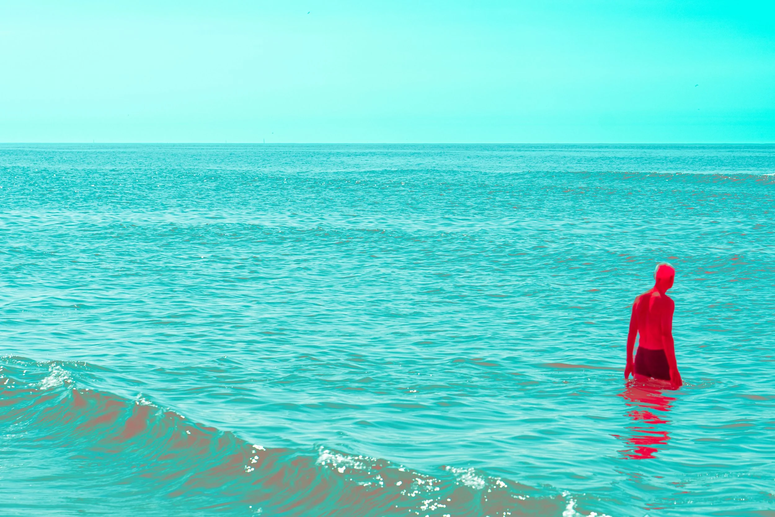 A person standing in the ocean near the shore, with a red filter overlay, and a clear horizon in the background.