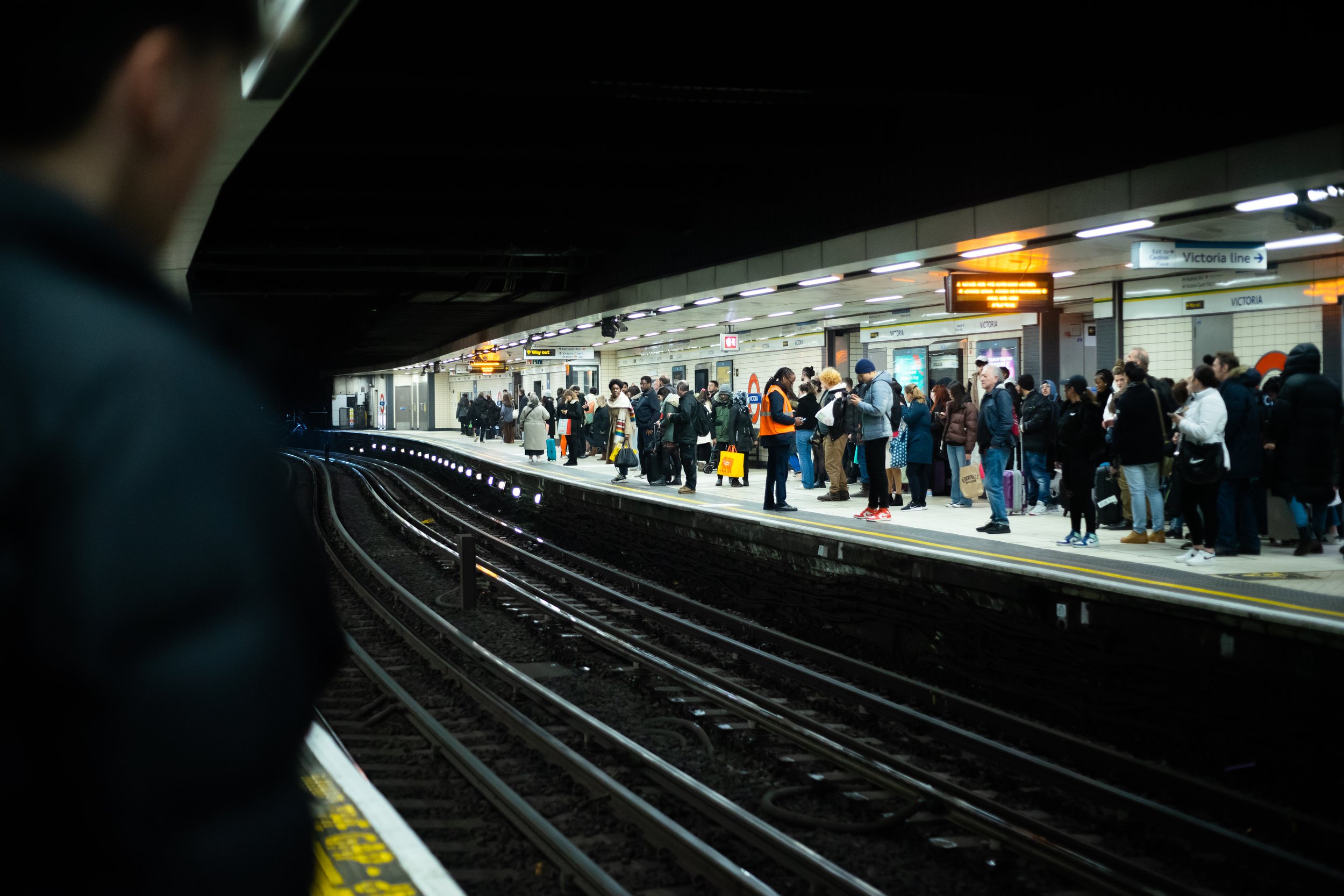 Crowded underground subway station platform with passengers waiting for the train, modern lighting, and signage overhead.
