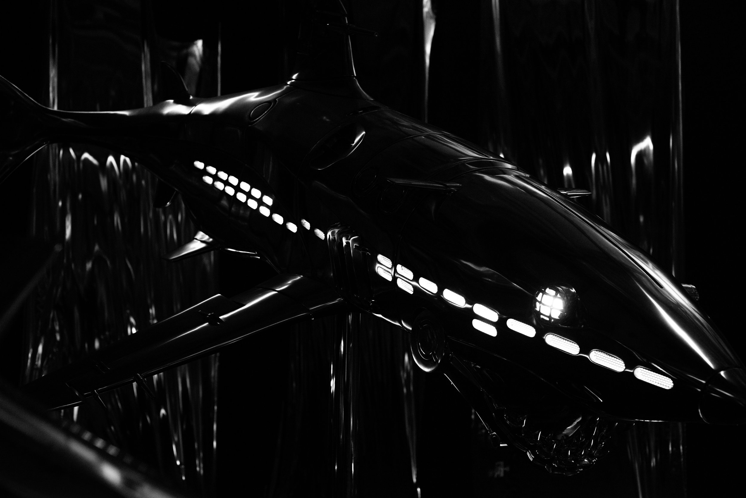 A model of a futuristic spaceship or aircraft with lights along its body, set against a dark, reflective background.