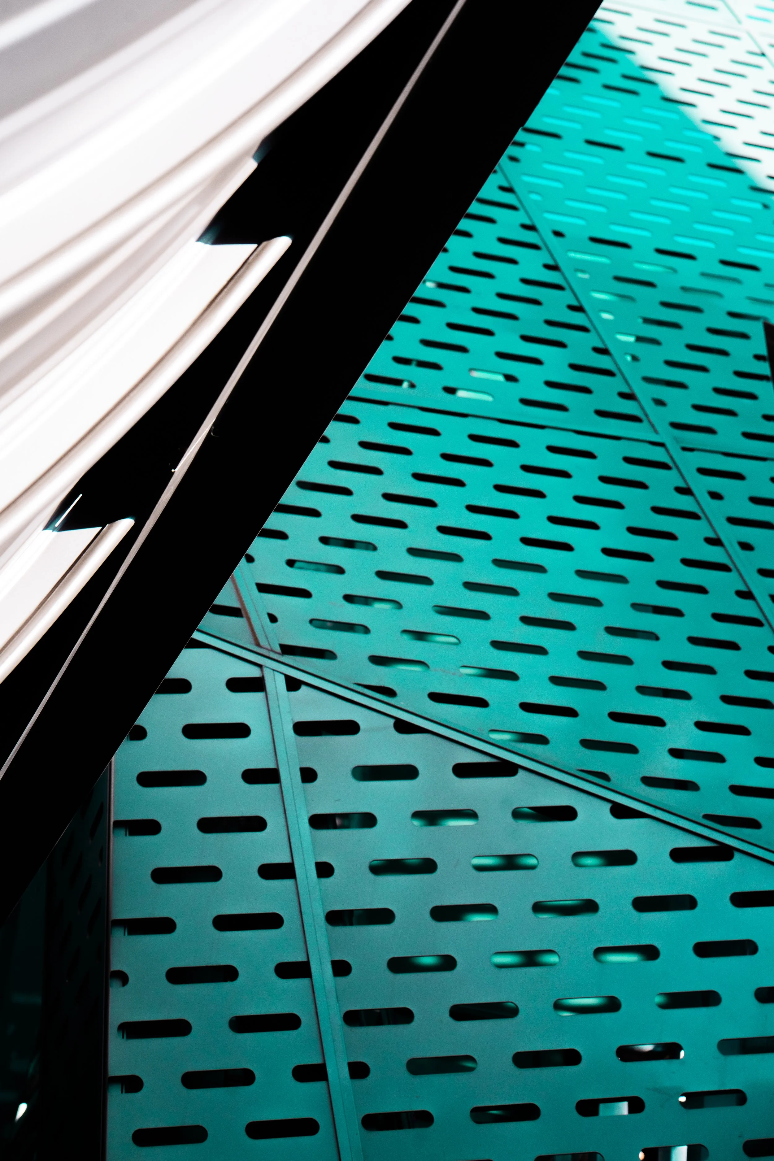 Close-up of a modern architectural facade with perforated turquoise metal panels and white horizontal louvers.