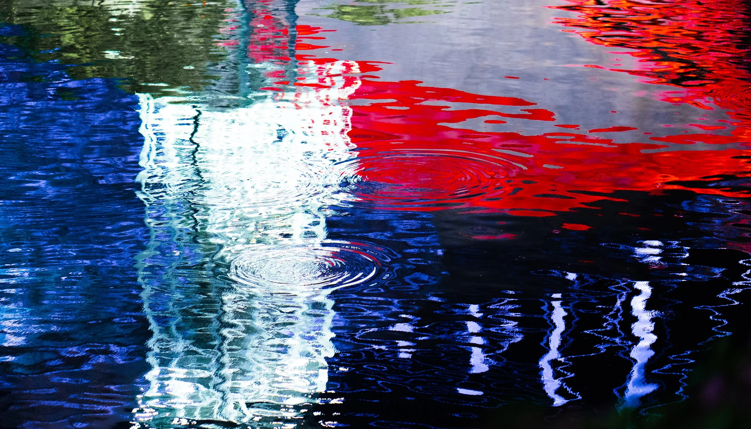 Reflections of a red, white, and blue American flag in water with ripples.