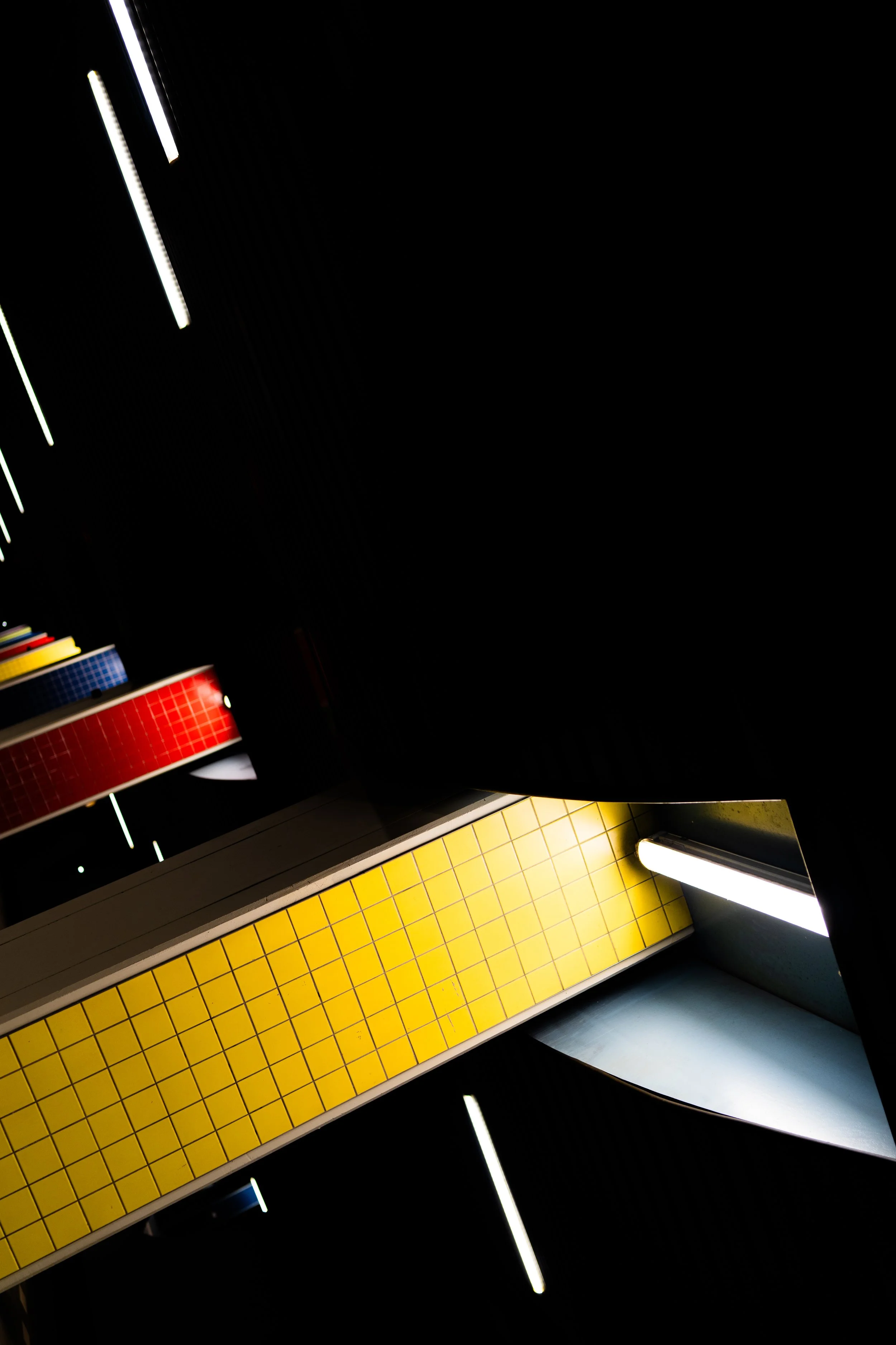 Interior view of a modern building shaft with a yellow tiled wall, fluorescent lighting, and dark surroundings.