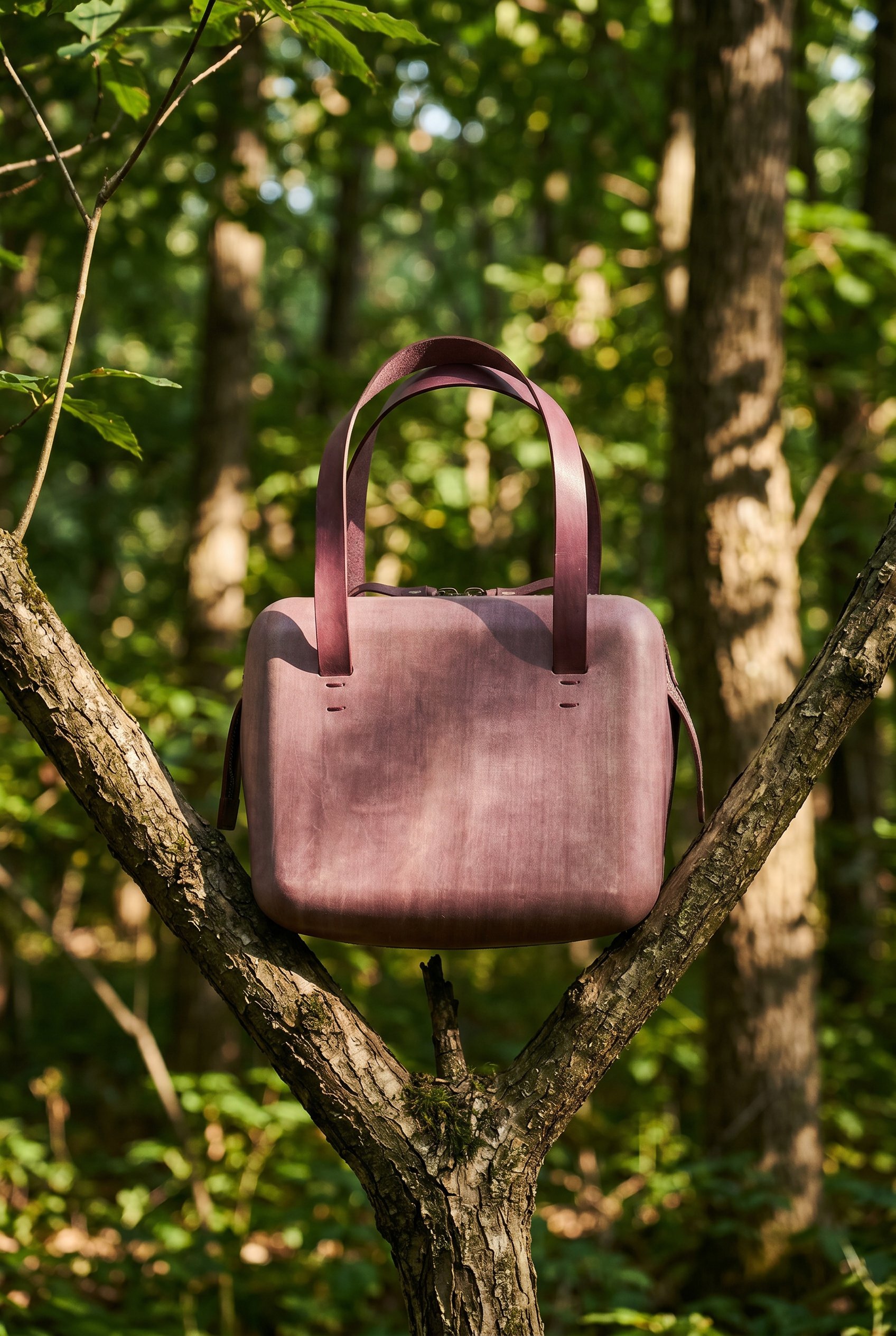 A pink handbag hanging on a tree branch in a forest with green leaves.