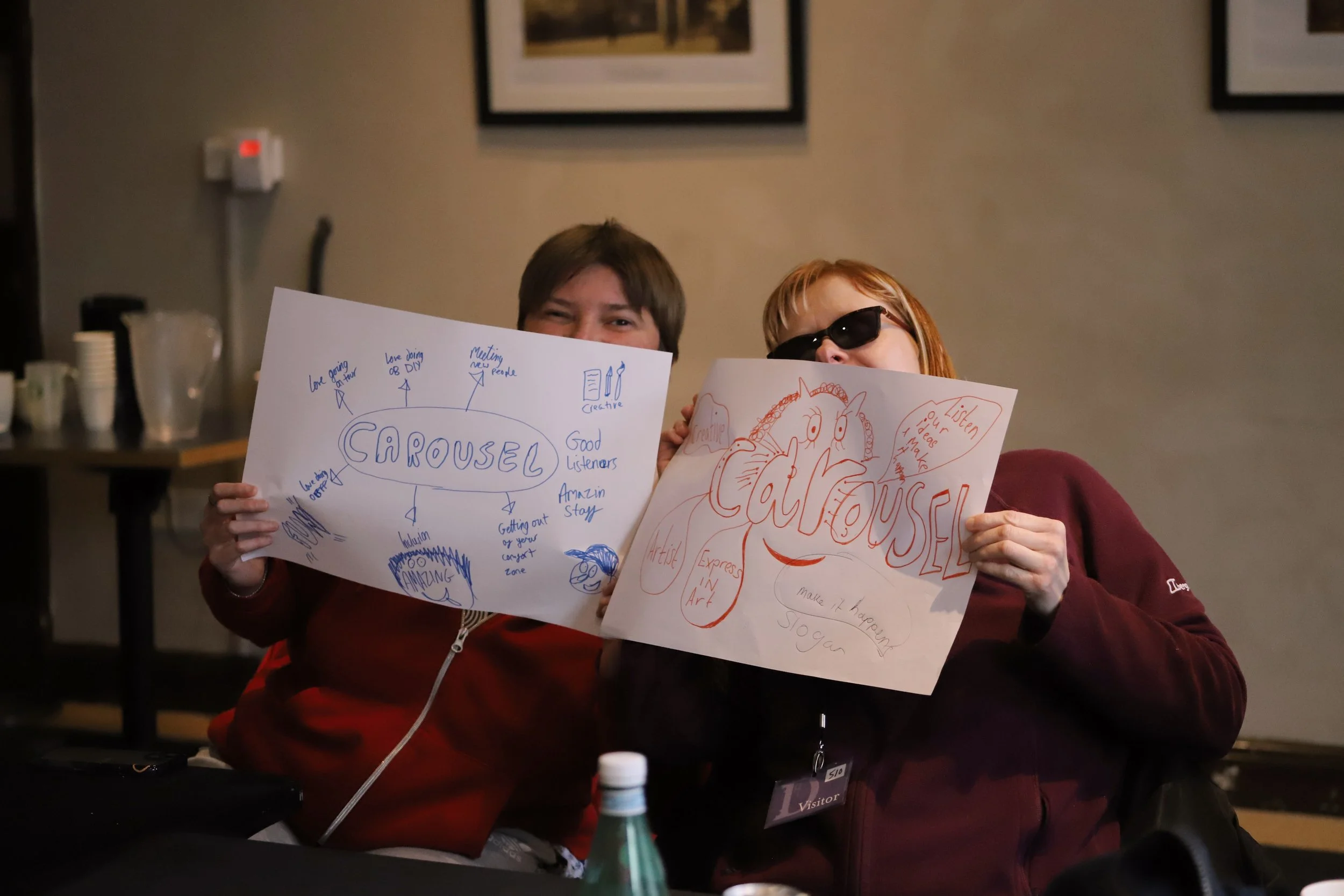 Kirsty Pentecost and Sarah Watson sit at a table, holding A3 mind maps. Kirsty’s is drawn in blue, Sarah’s is in orange.
