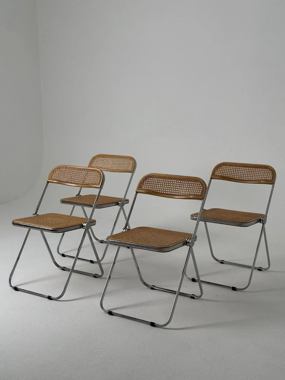 Four folding chairs with rattan seats and backs, arranged in a row against a plain white background.