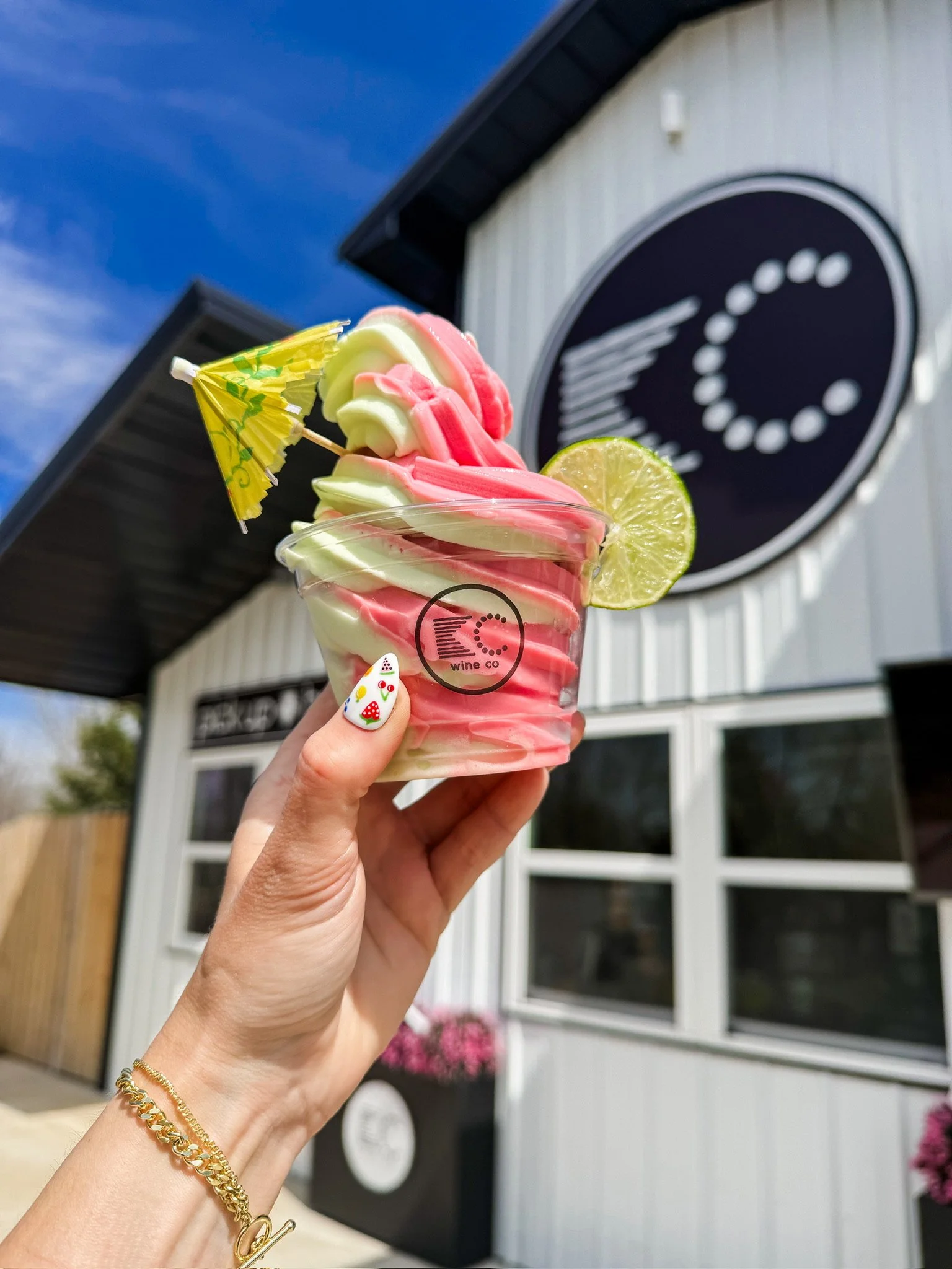 Hand holding lime and strawberry twisted soft serve margarita with an umbrella and lime slice decor.