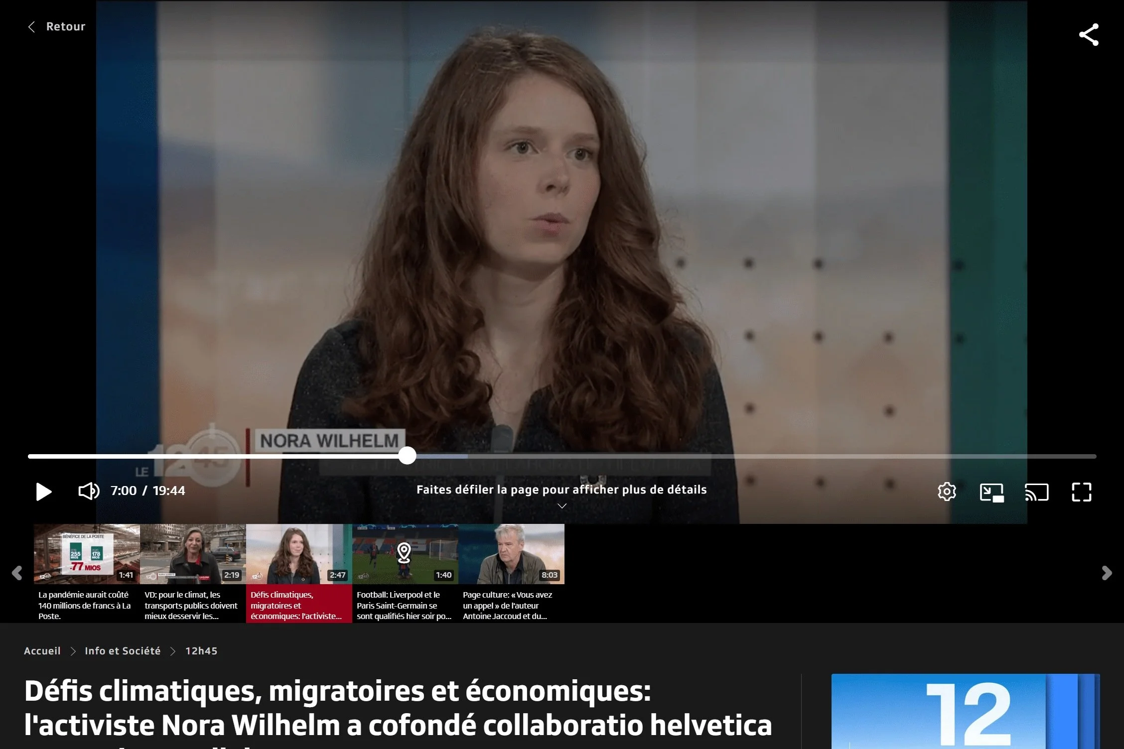 A woman with long, wavy red hair speaking at a news interview. The caption on the screen says Nora Wilhelm. The background features a metallic wall with small rivets.