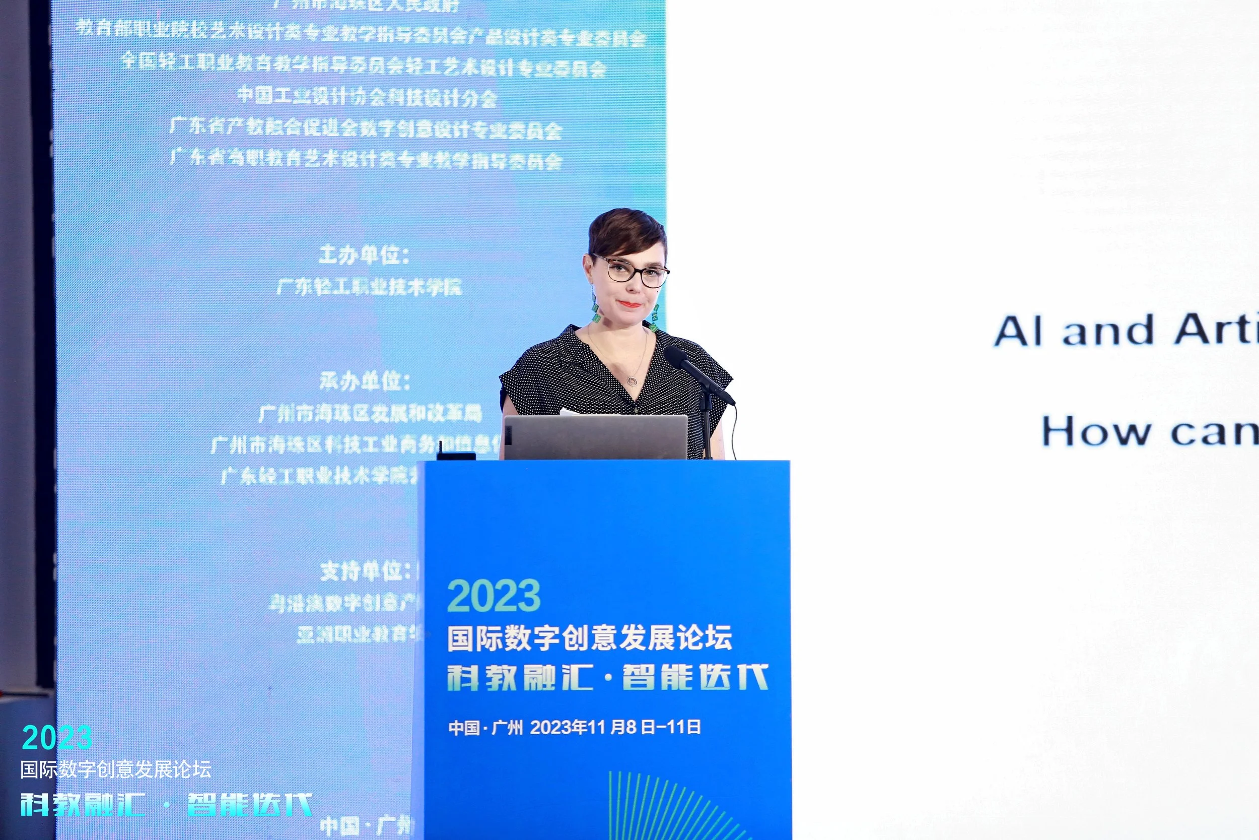 A woman speaking at a podium during a conference, with a large digital screen behind her displaying event information in Chinese text and the event title in English, 'AI and Art'.
