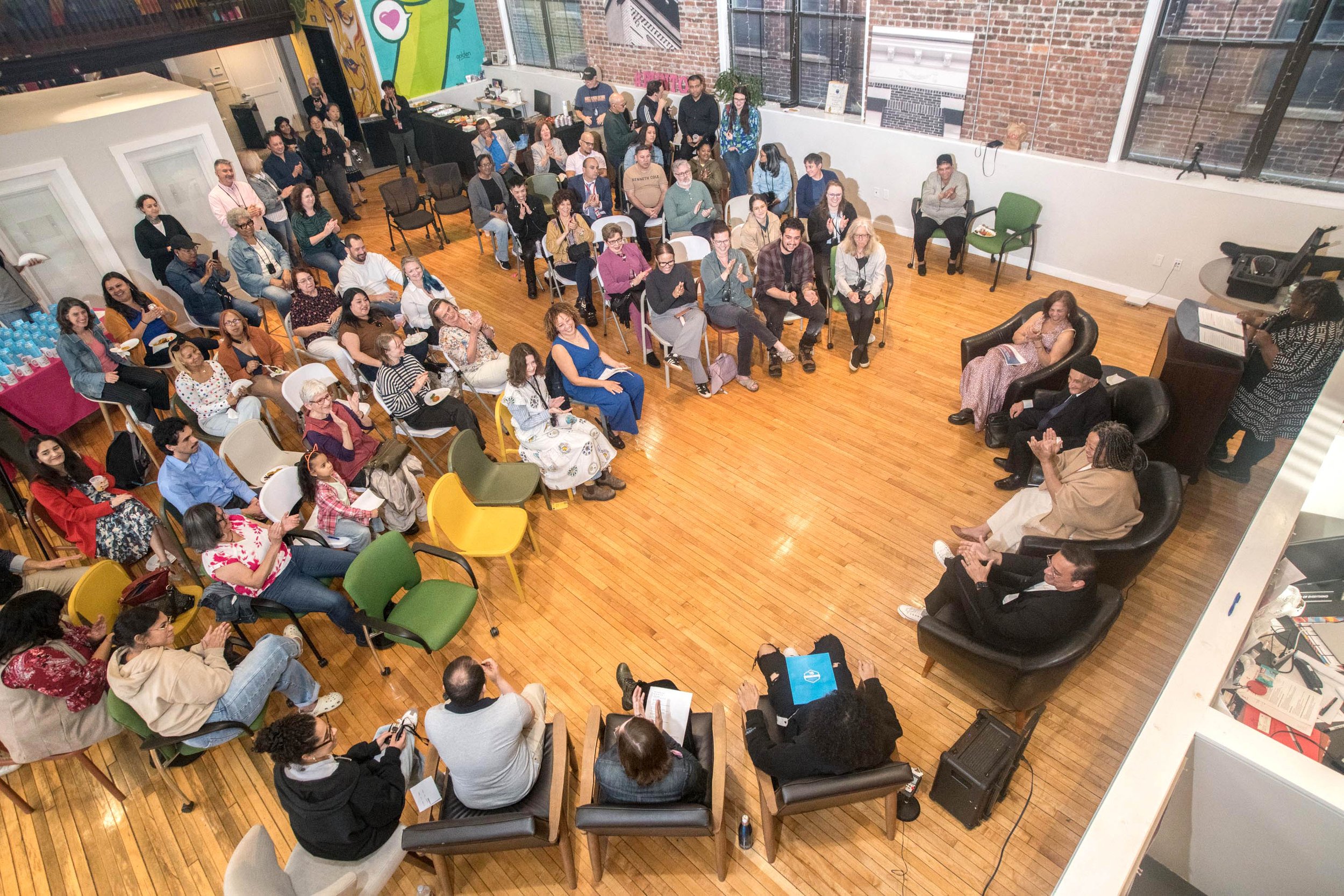 Audience attending a panel discussion in a loft-style venue with wooden floors, brick walls, and large windows.