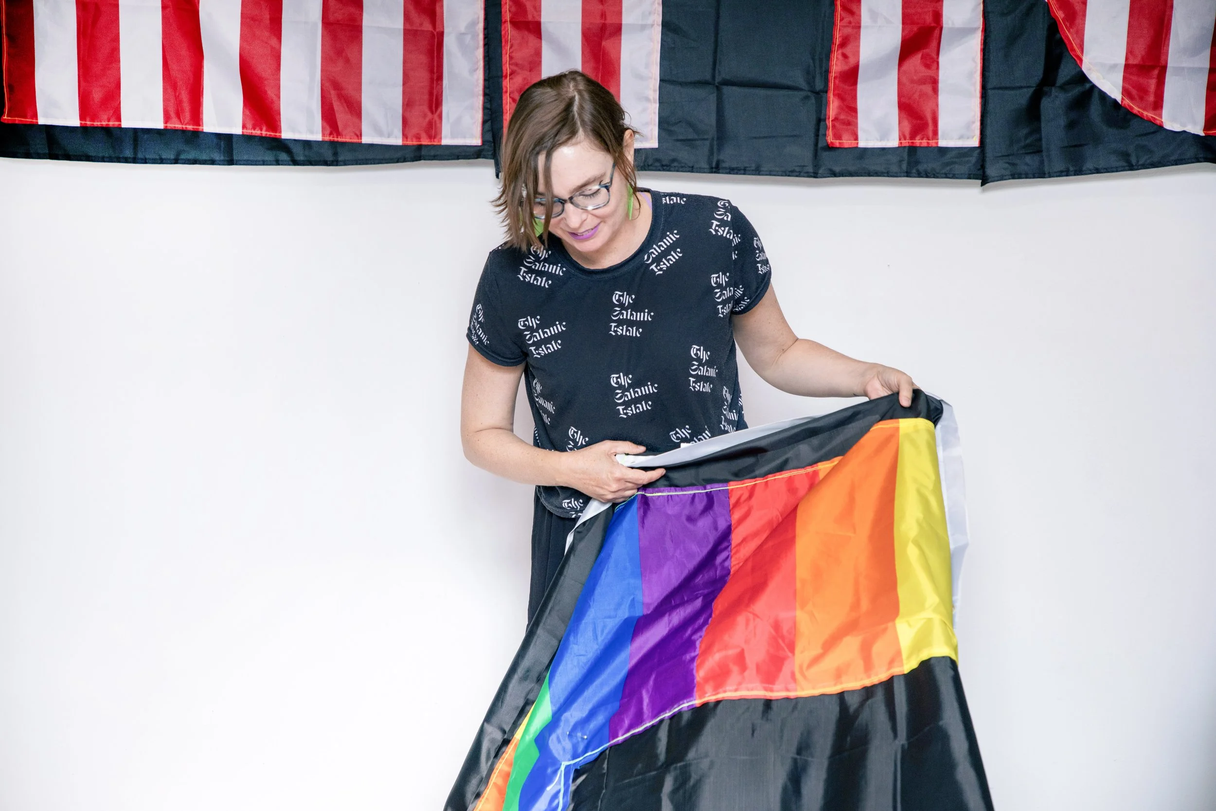 A woman holding a rainbow pride flag with a black background and red and white flags hanging above