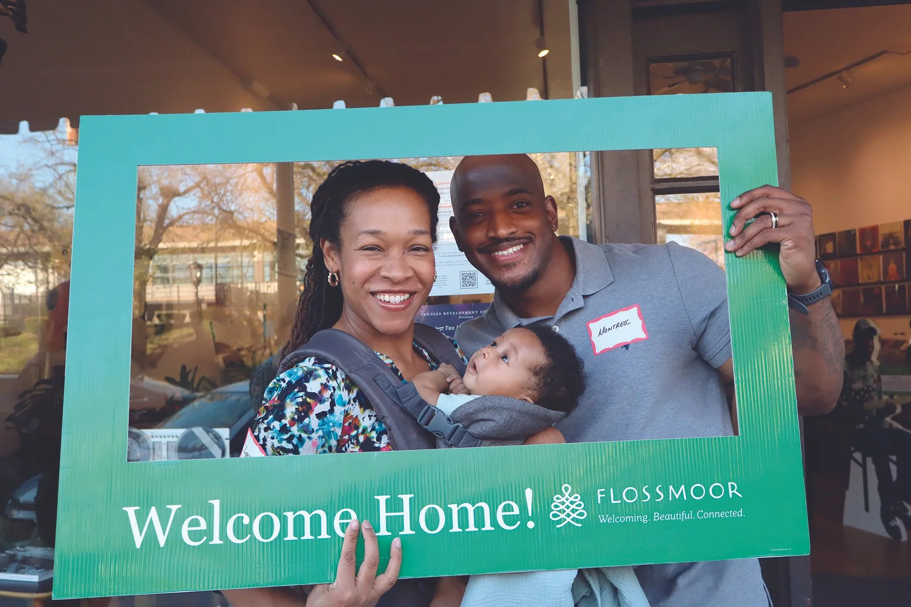 A smiling couple holding a newborn baby look through a Welcome Home sign
