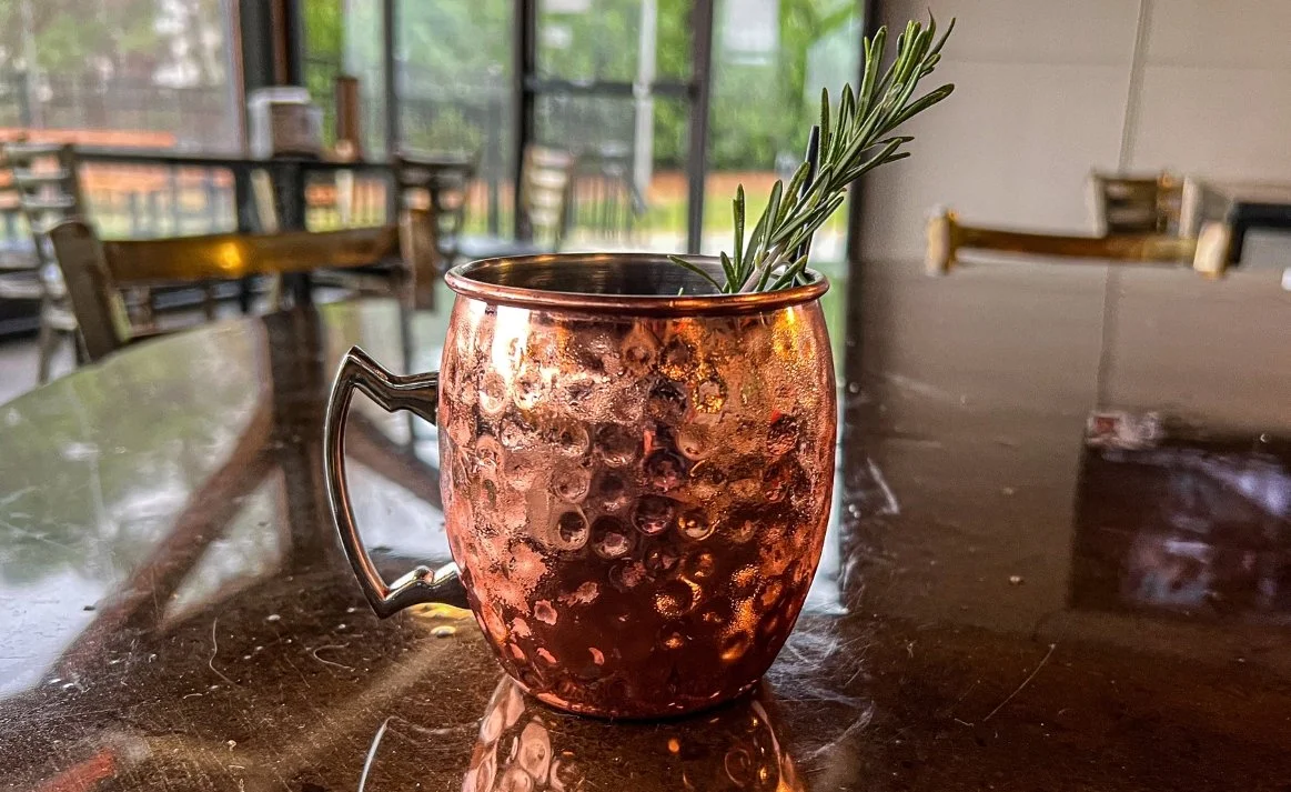Rudolph the Red-Nosed Mule from Moscow cocktail from Royal Bliss with vodka, orange liqueur, ginger beer, and pomegranate juice with a fresh rosemary garnish served in a copper mug.