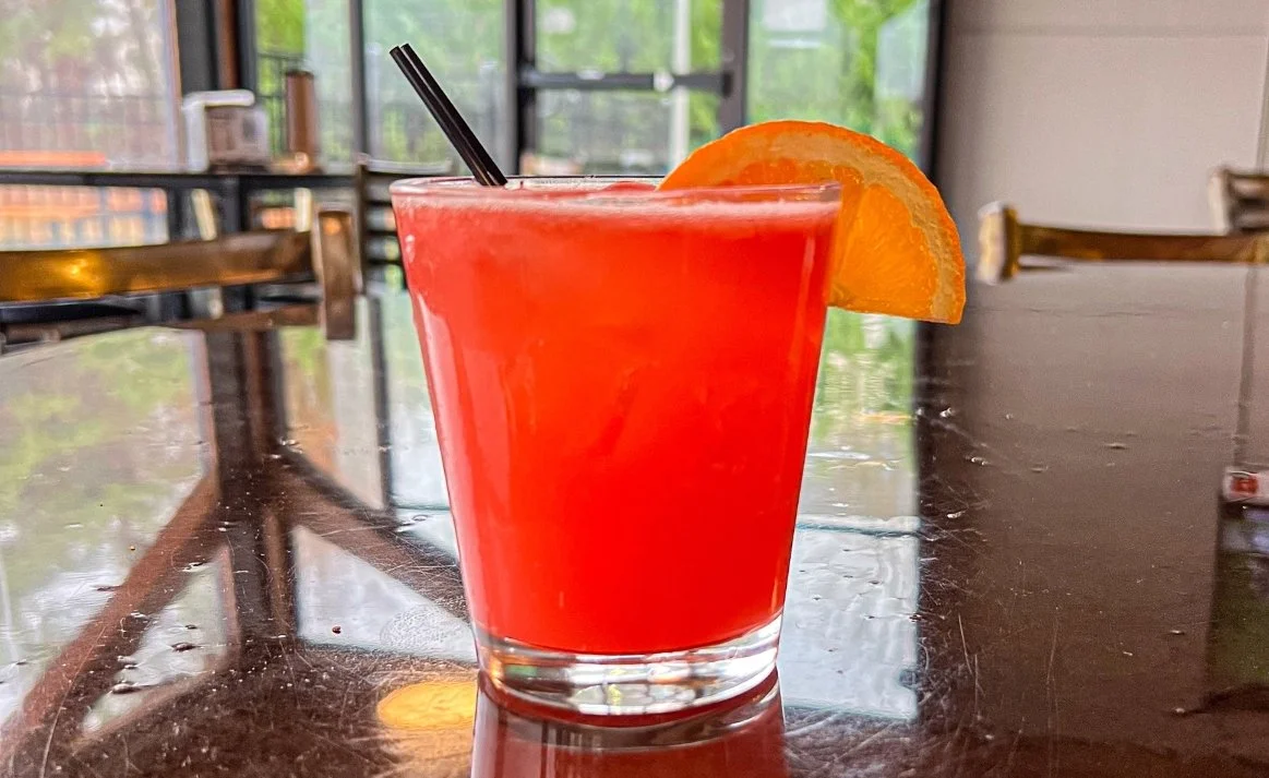 Happy Y’allidays cocktail from Royal Bliss with tequila, orange juice, cranberry juice, grenadine, and lime juice topped with club soda and orange slice garnish.