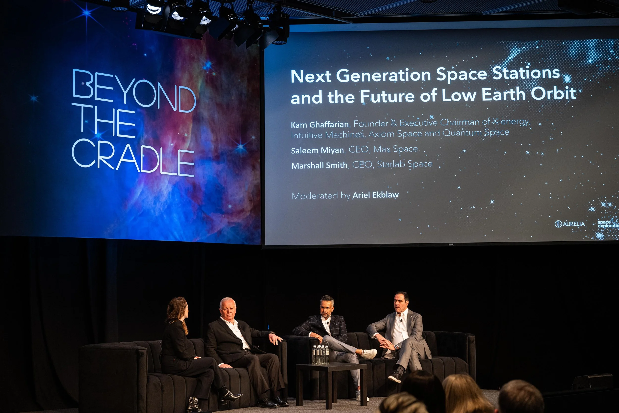 ALT TEXT: A panel at Aurelia Institute's Beyond the Cradle 10th Anniversary conference with four speakers on stage. The title of the session on the large screen in the background is, "Next Generation Space Stations, and the Future of Low Earth Orbit.