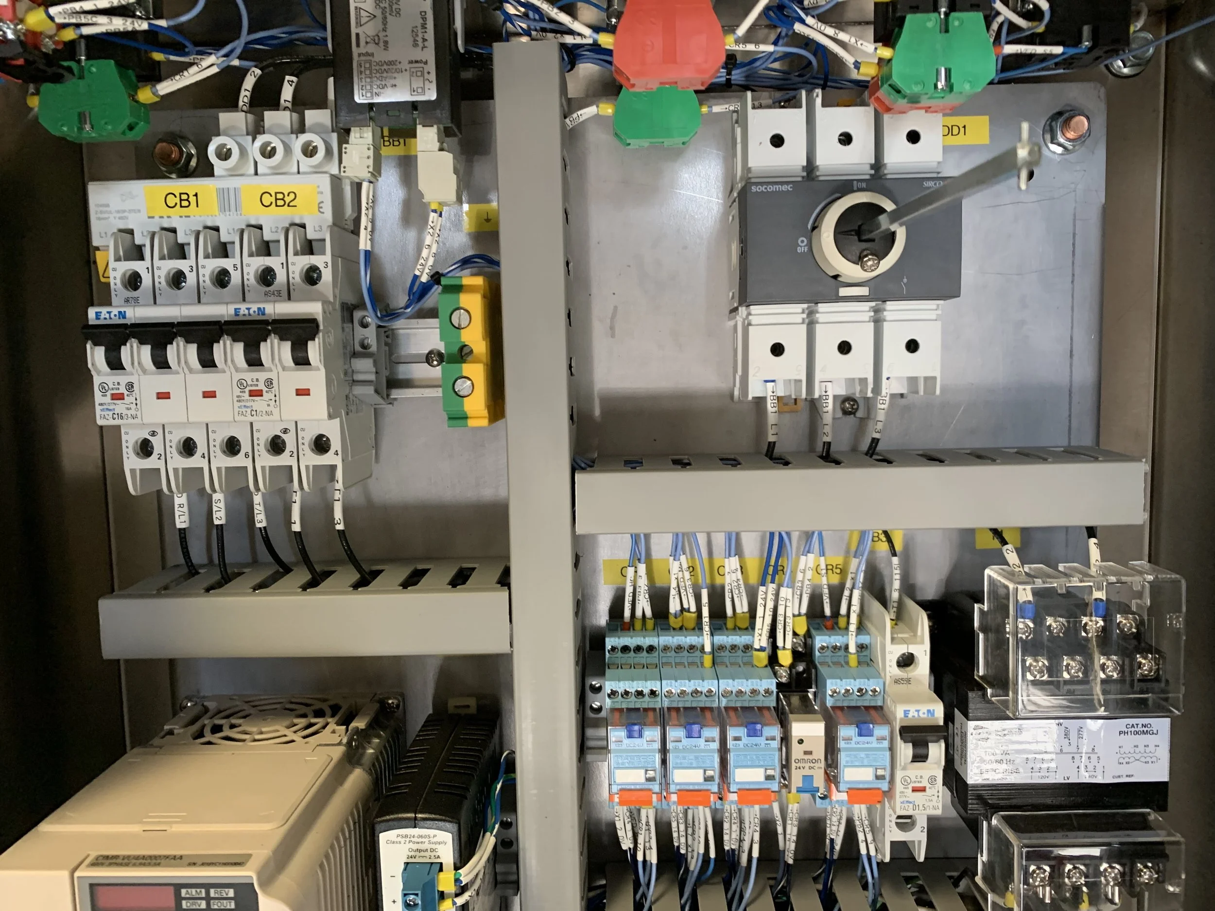 An industrial electrical control panel with various wires, switches, circuit breakers, and relays organized inside a metal enclosure.