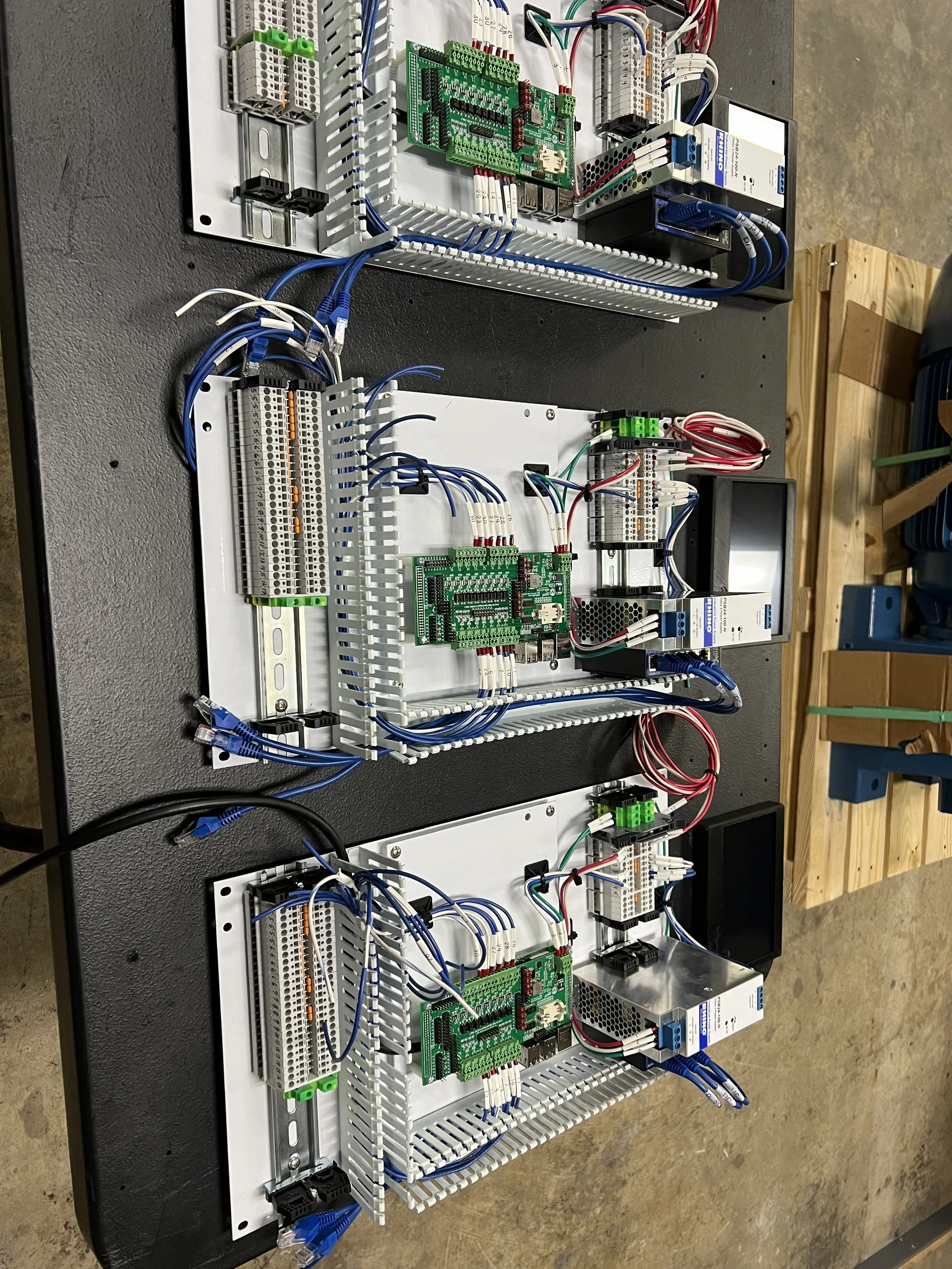 Electrical control panels with circuit boards, wiring, power supplies, and terminal blocks mounted on white panels on a black work surface.