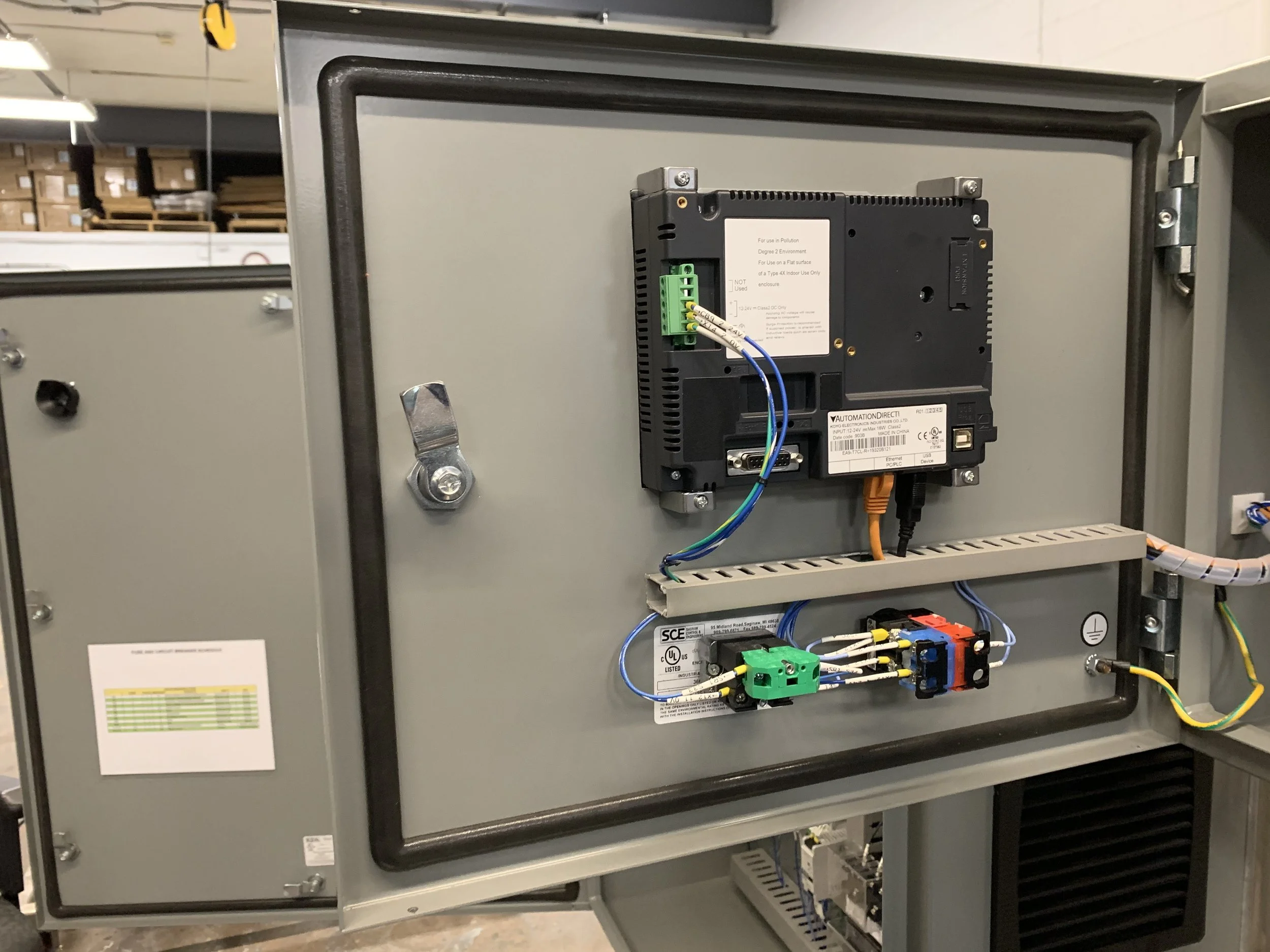 Electronic control panel inside an industrial metal enclosure, with various wires connected to green terminal blocks and labeled components.