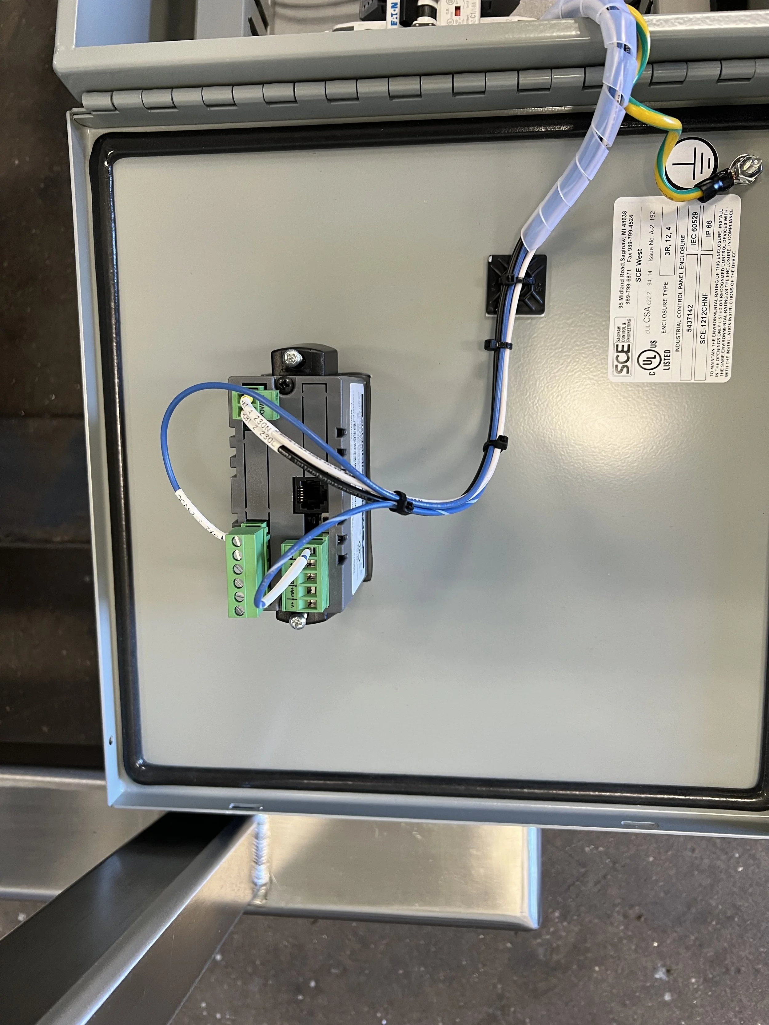 Interior of an electrical control panel with wires and components inside a metal enclosure, on a workshop floor.