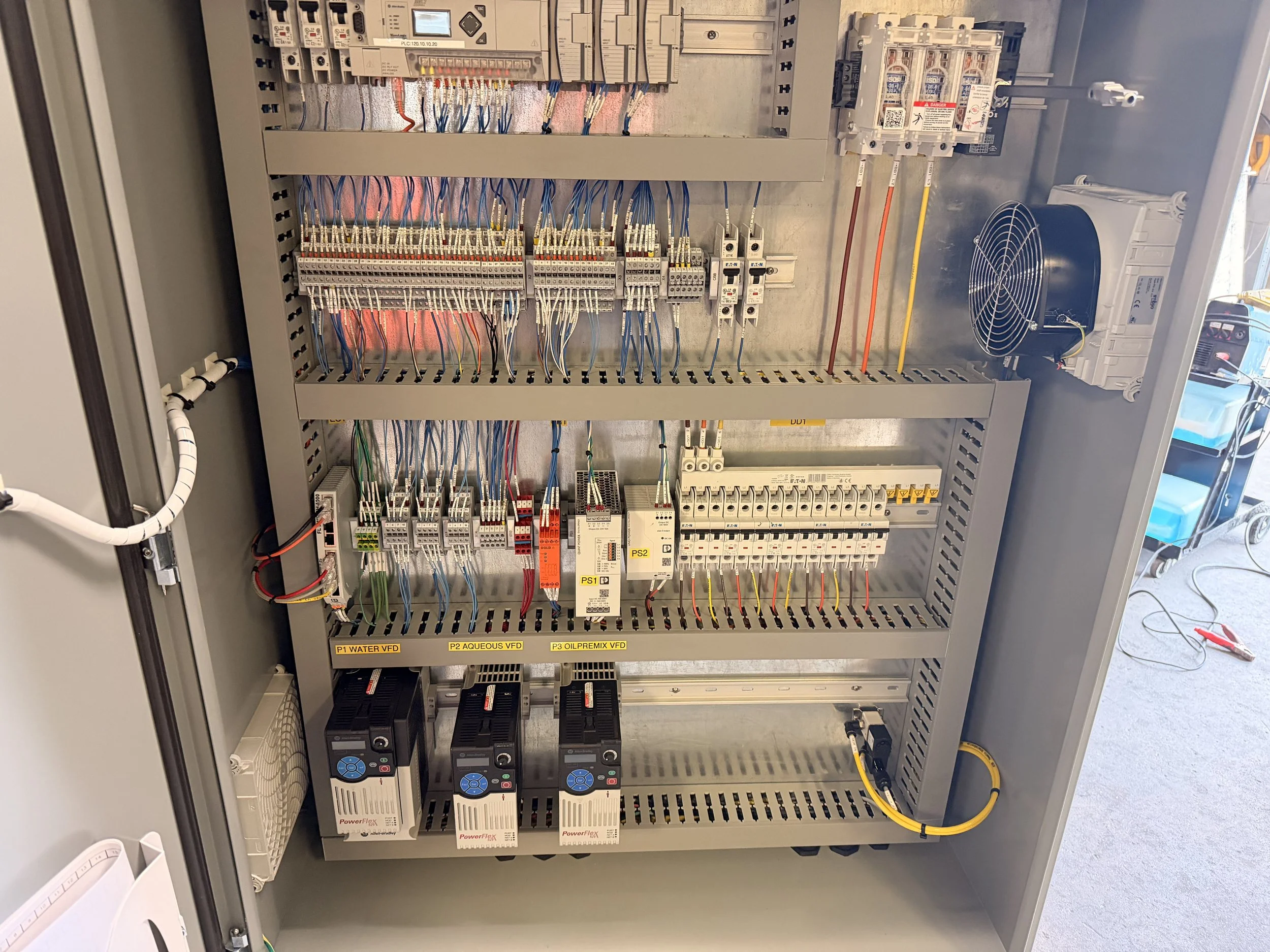 An open electrical control panel with various wires, circuit breakers, and electronic components labeled for different functions such as water, aqueous, and oil premix vortex flow devices.
