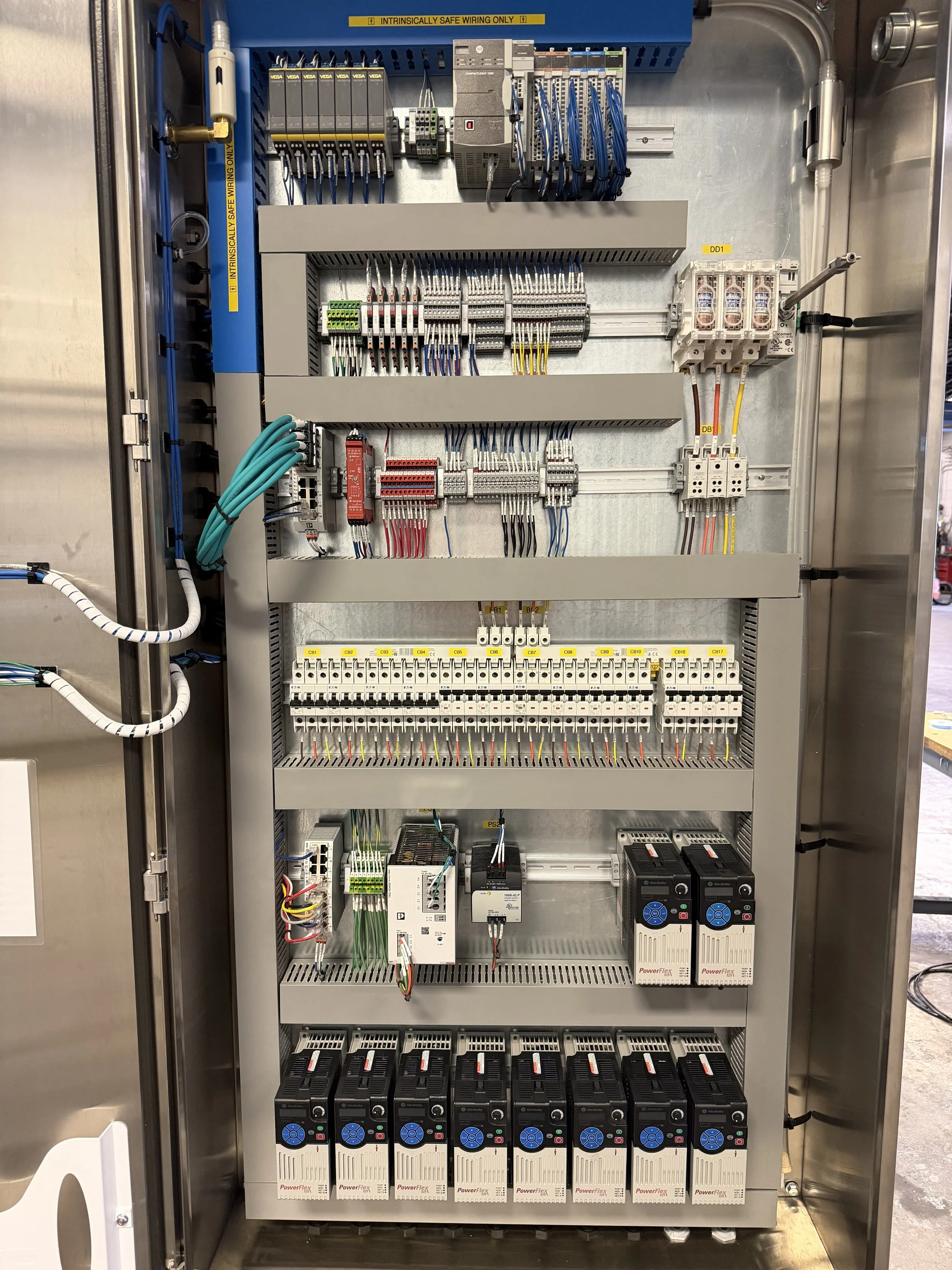Electrical control panel with various circuit breakers, wires, and industrial components mounted inside a metal enclosure.