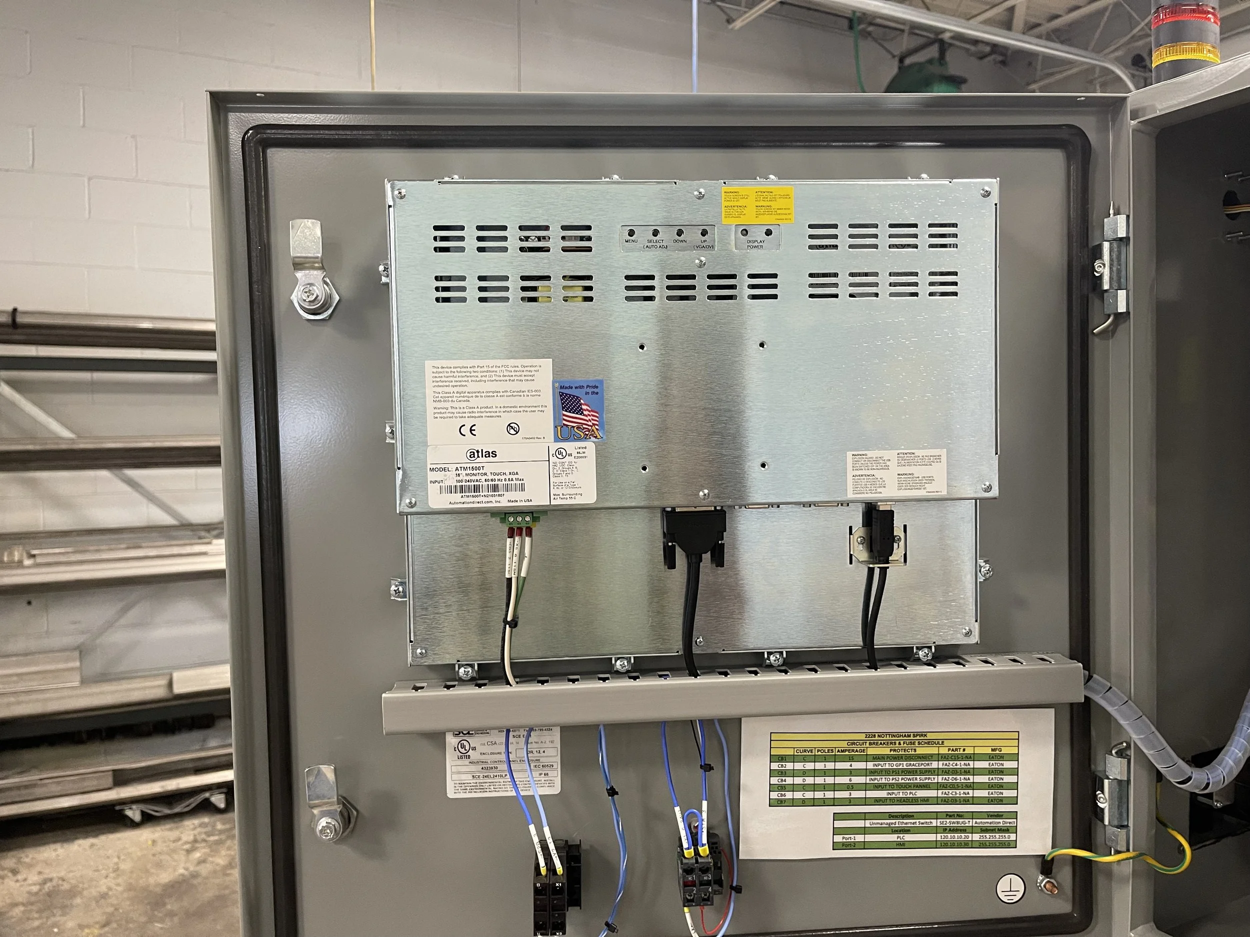 An electrical control panel mounted inside a metal enclosure, with various wires, labels, and circuit breakers visible.